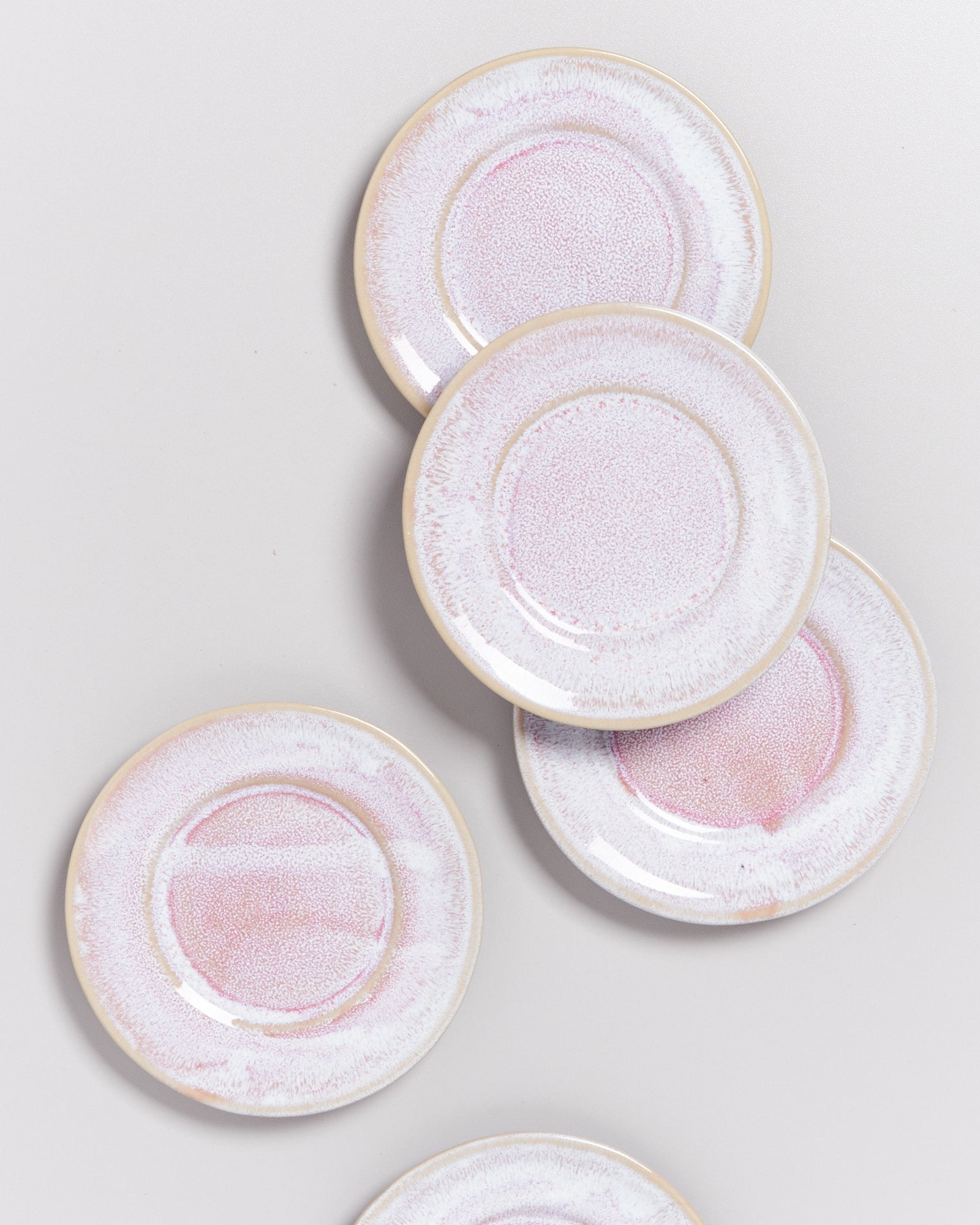 Fünf runde, rosafarbene Teller mit einem gesprenkelten Muster liegen auf einer hellgrauen Oberfläche.