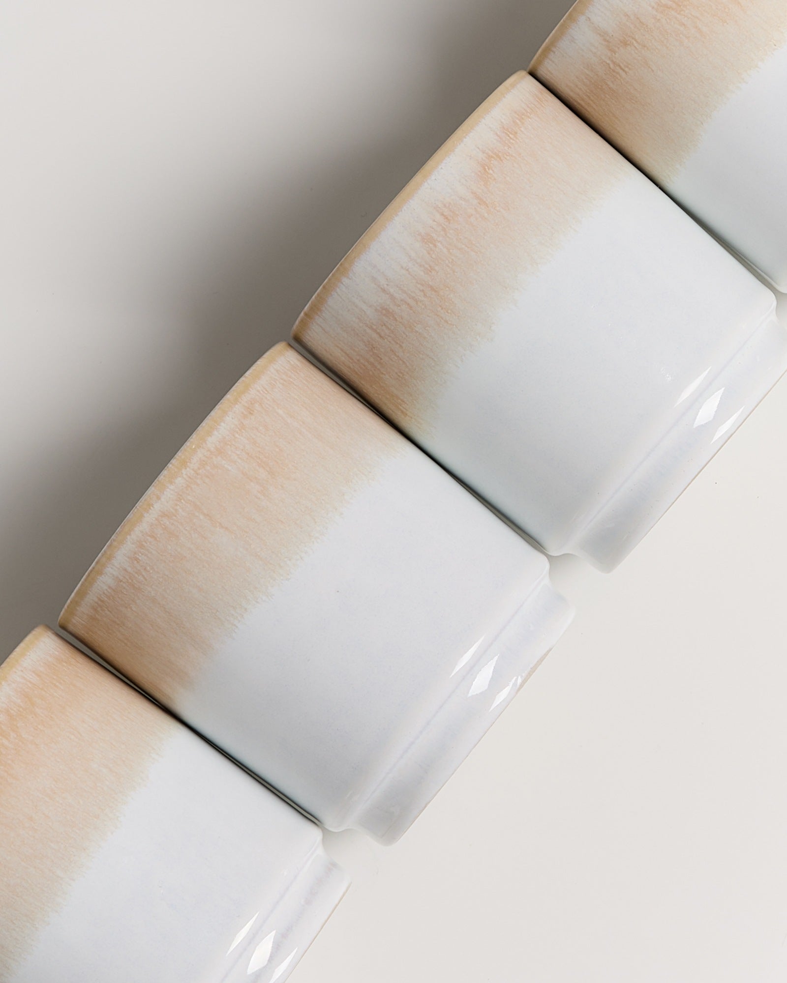 Vier weiße Tassen mit hellbrauner Streifenmusterung, nahe beieinander aufgestellt.