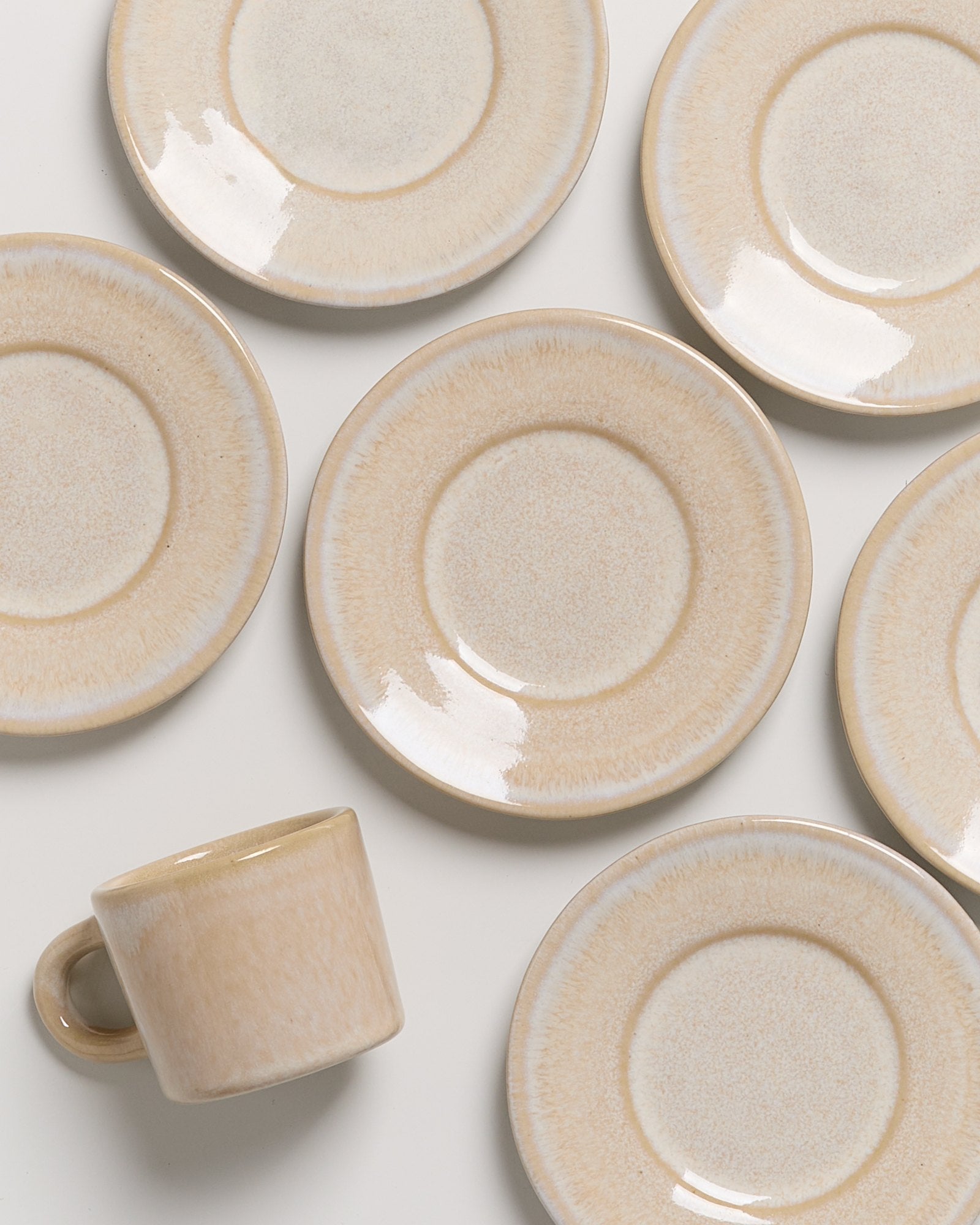 Beige Tasse und sieben passende Teller auf hellem Hintergrund angeordnet.