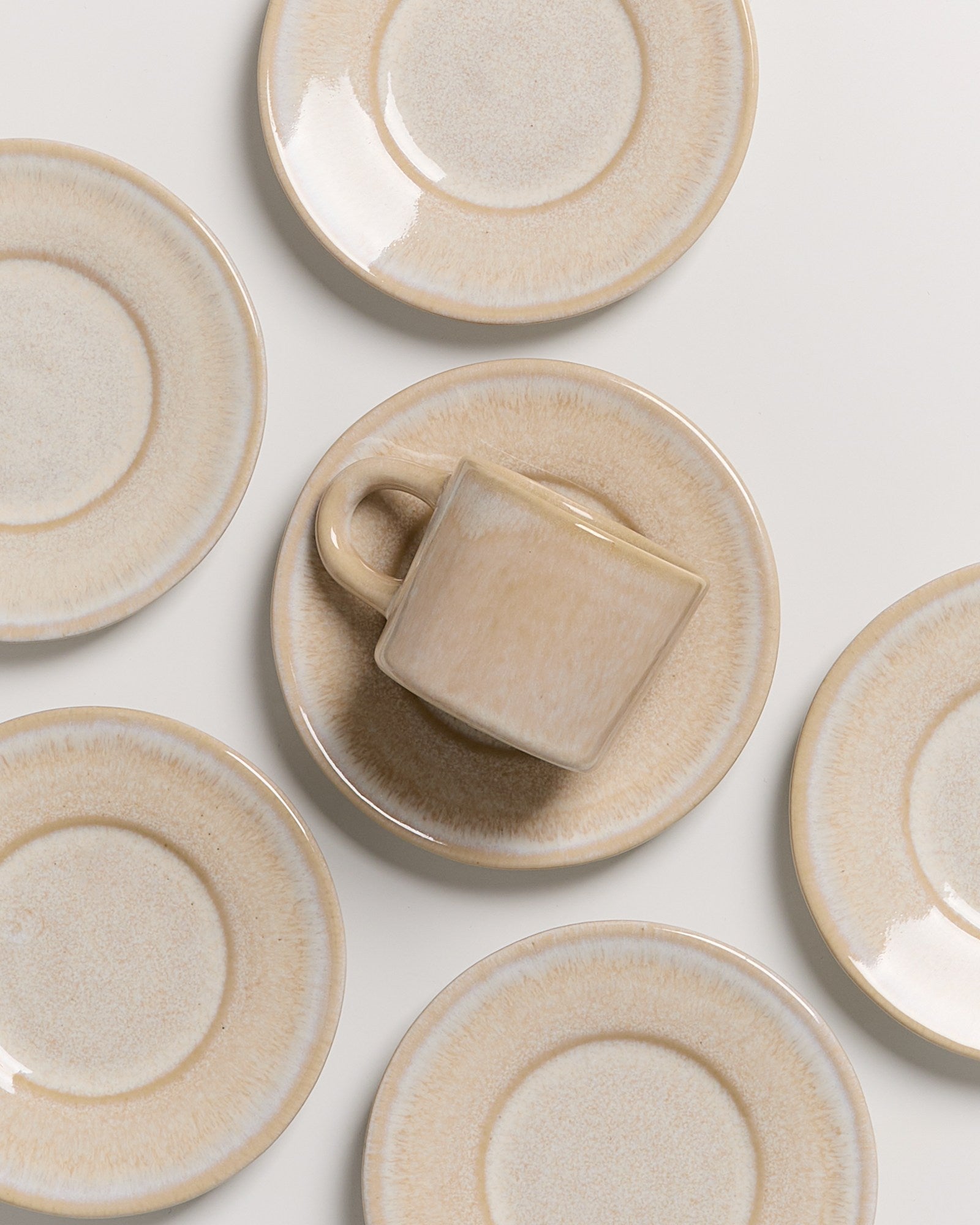 Sechs beigetönige Untertassen mit einer Tasse in der Mitte auf weißem Hintergrund angeordnet.