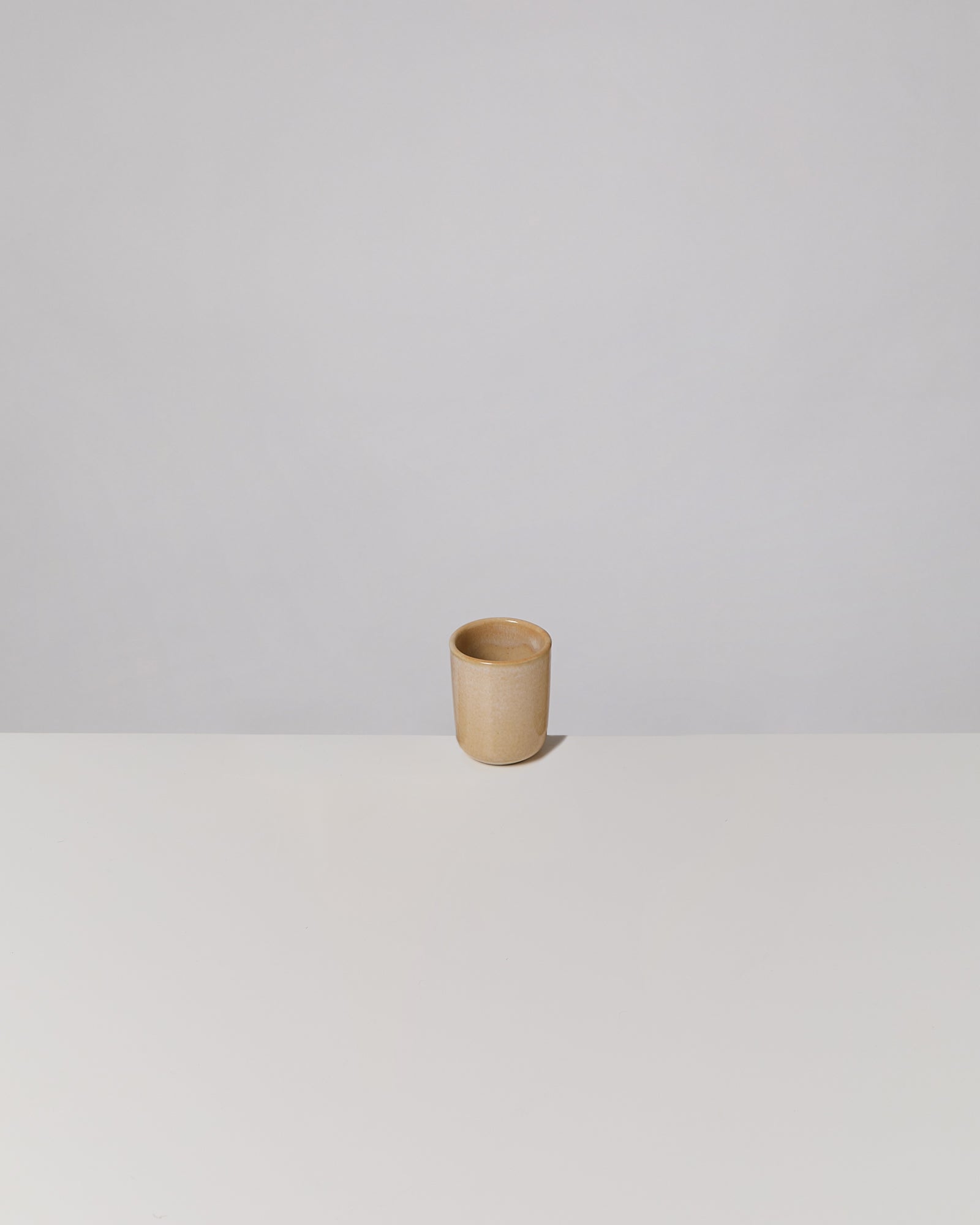 Brauner Becher auf weißem Tisch vor einem grauen Hintergrund.