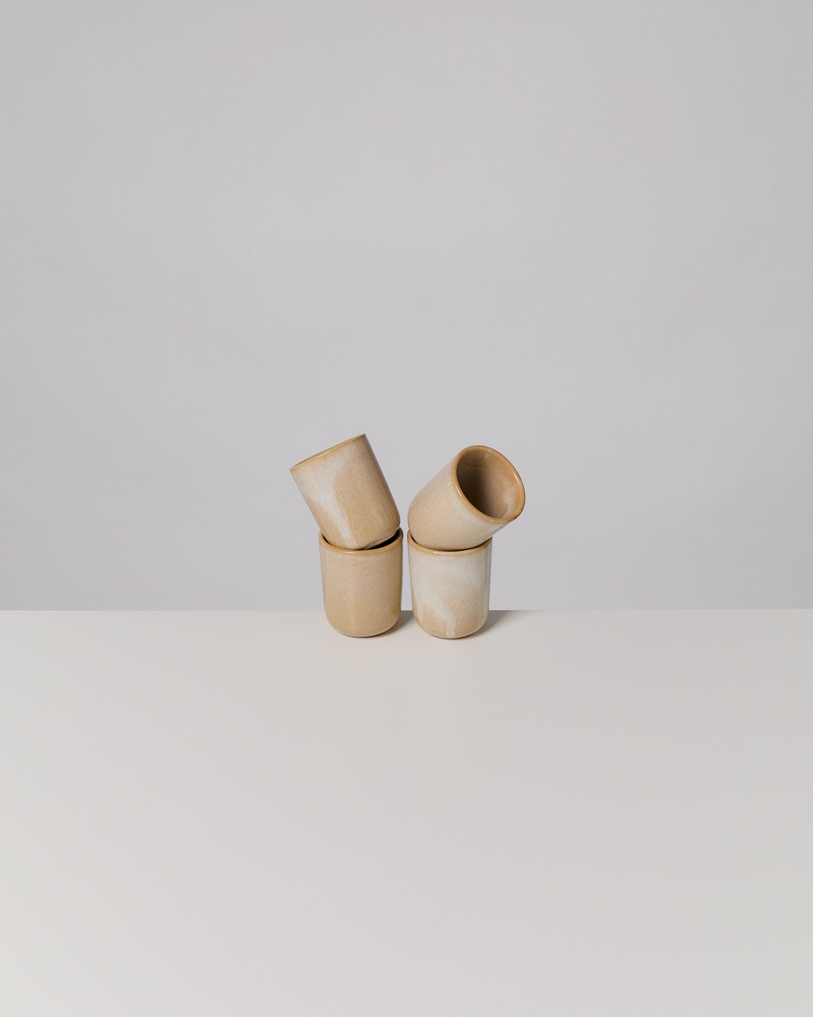 Vier beige Keramikbecher stehen auf einem weißen Tisch, zwei davon sind schräg aufeinander gestapelt.