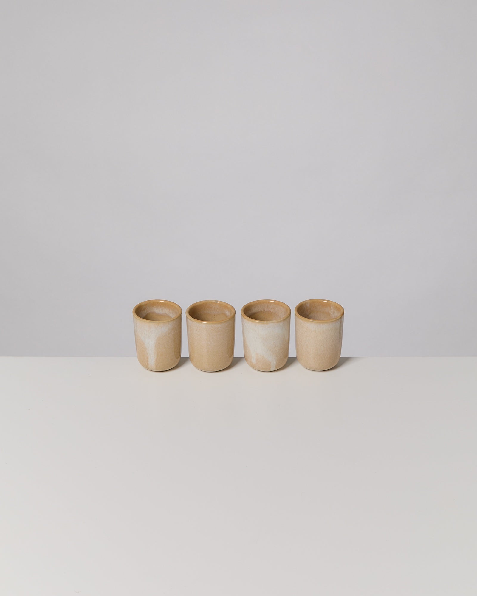 Vier beige Keramiktassen stehen auf einem weißen Tisch in einer Reihe.