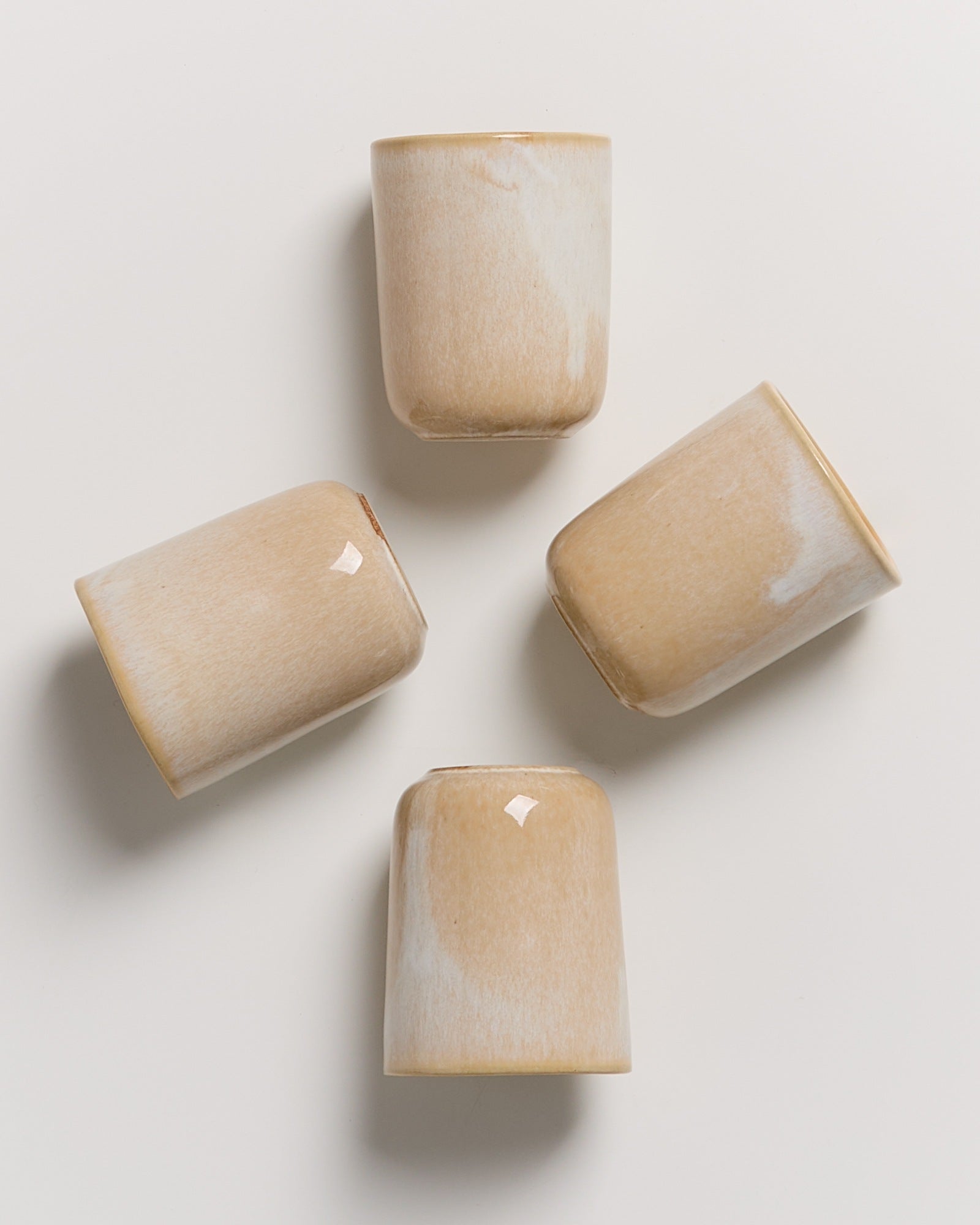 Vier beige-weiße Keramiktassen liegen in einem Muster auf einem weißen Hintergrund.