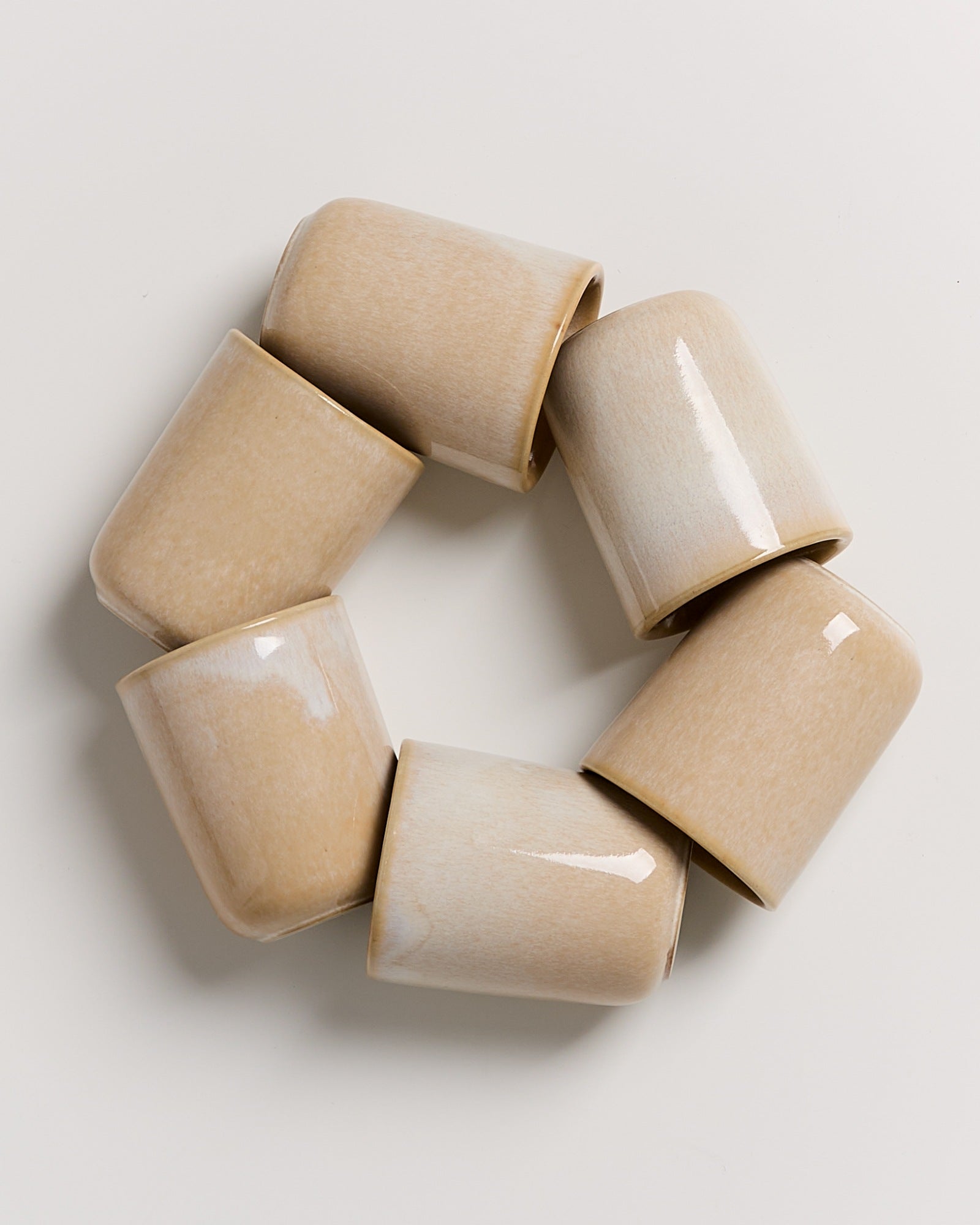 Sechs becherförmige, beige Keramikteile bilden einen Ring auf einem weißen Hintergrund.