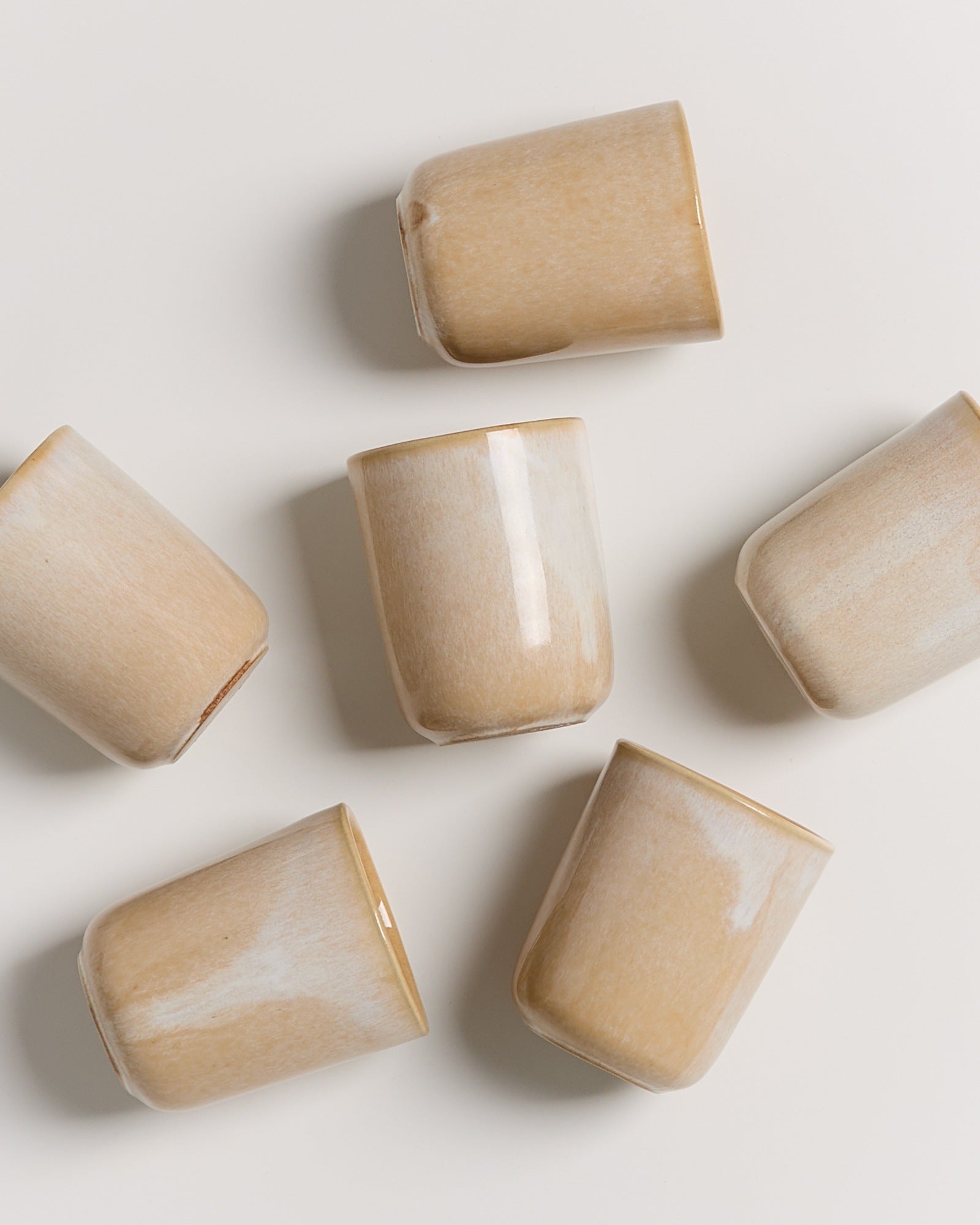 Sechs beige, kippende Keramiktassen auf einem weißen Hintergrund.