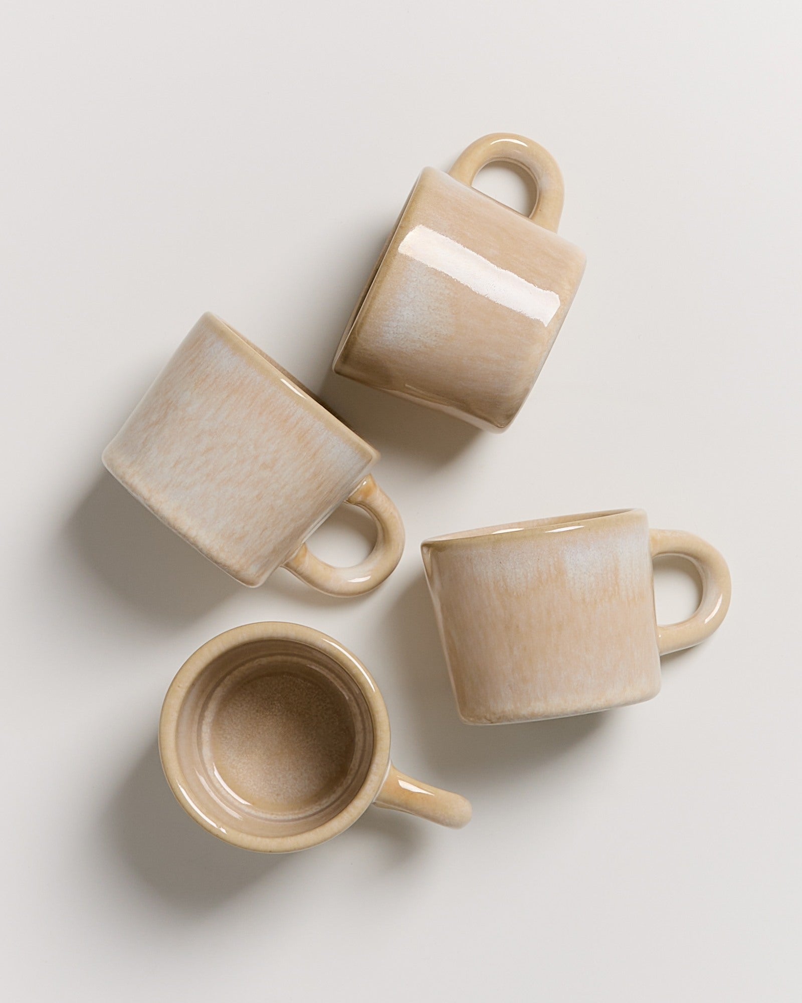 Vier beige Tassen liegen auf einer hellen Oberfläche.
