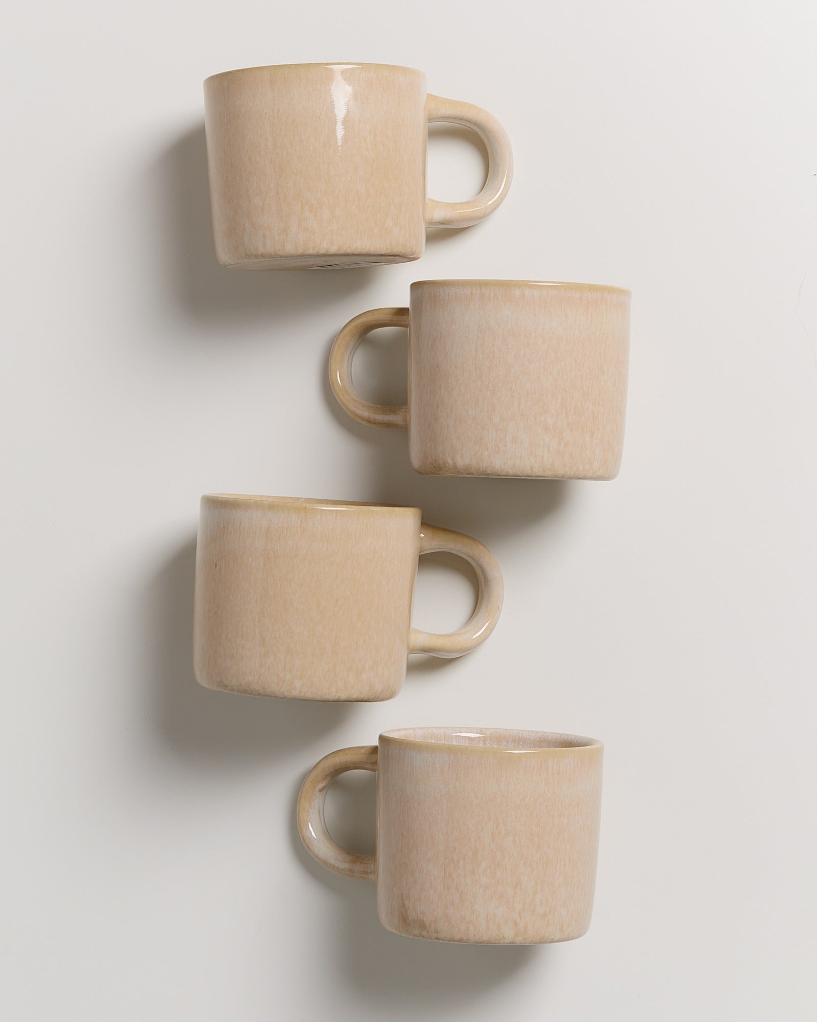 Vier beige Keramiktassen, gestapelt in einer vertikalen Reihe auf weißem Hintergrund.