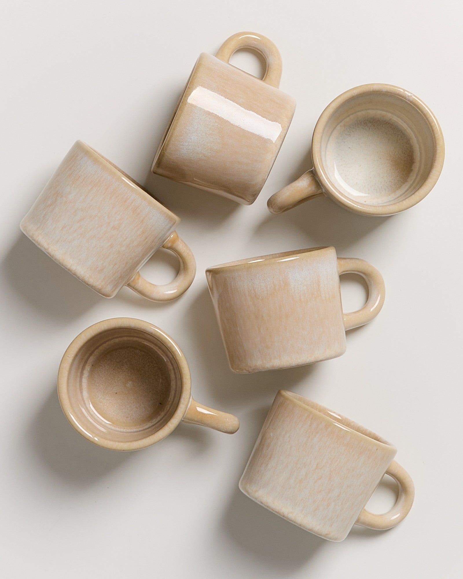 Sechs beigefarbene Kaffeetassen liegen auf einem weißen Hintergrund, einige stehen auf dem Kopf.