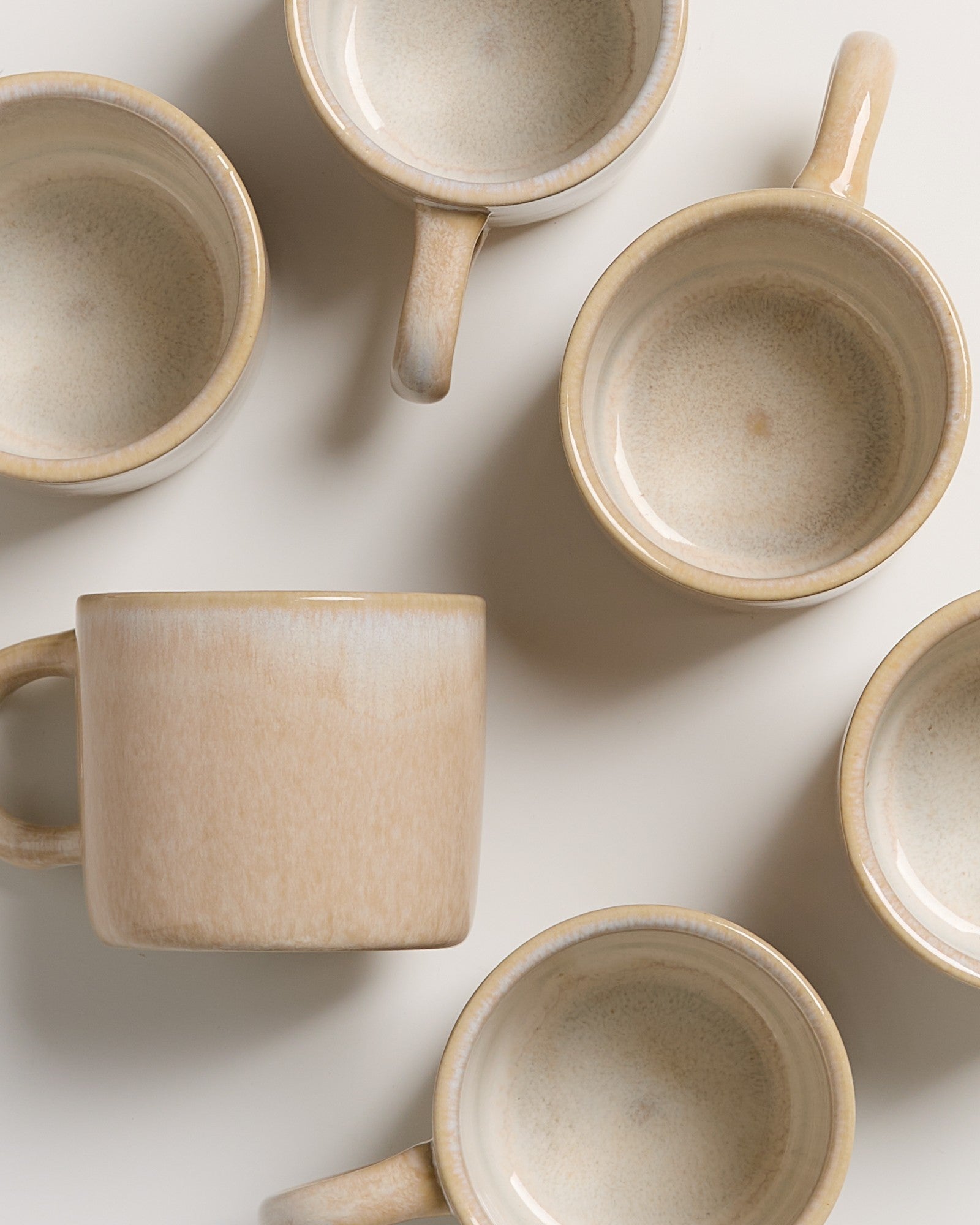 Sechs beige Tassen in verschiedenen Ausrichtungen auf einem hellen Hintergrund.