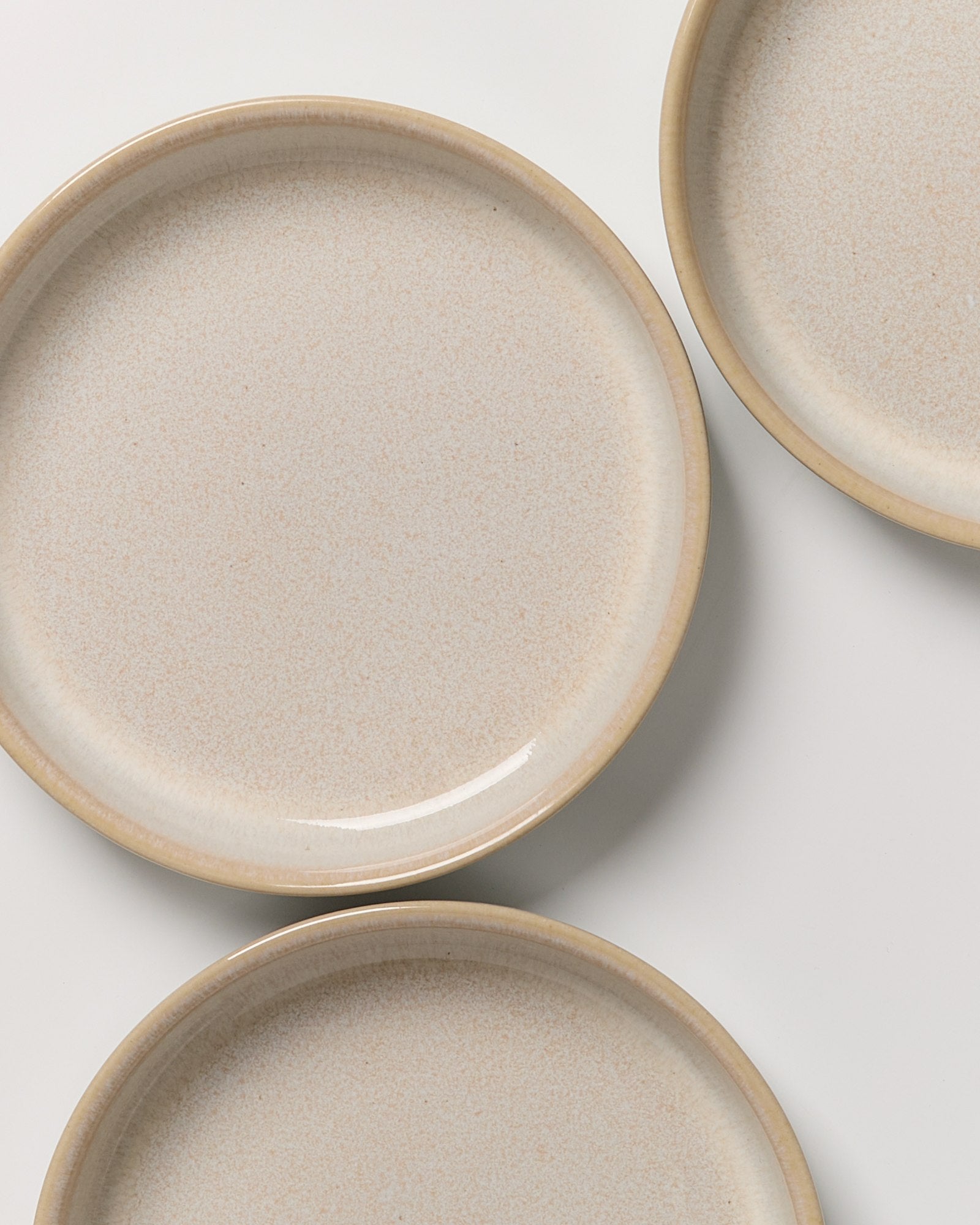 Drei beige Keramikteller mit leicht gesprenkelter Oberfläche auf weißem Hintergrund.