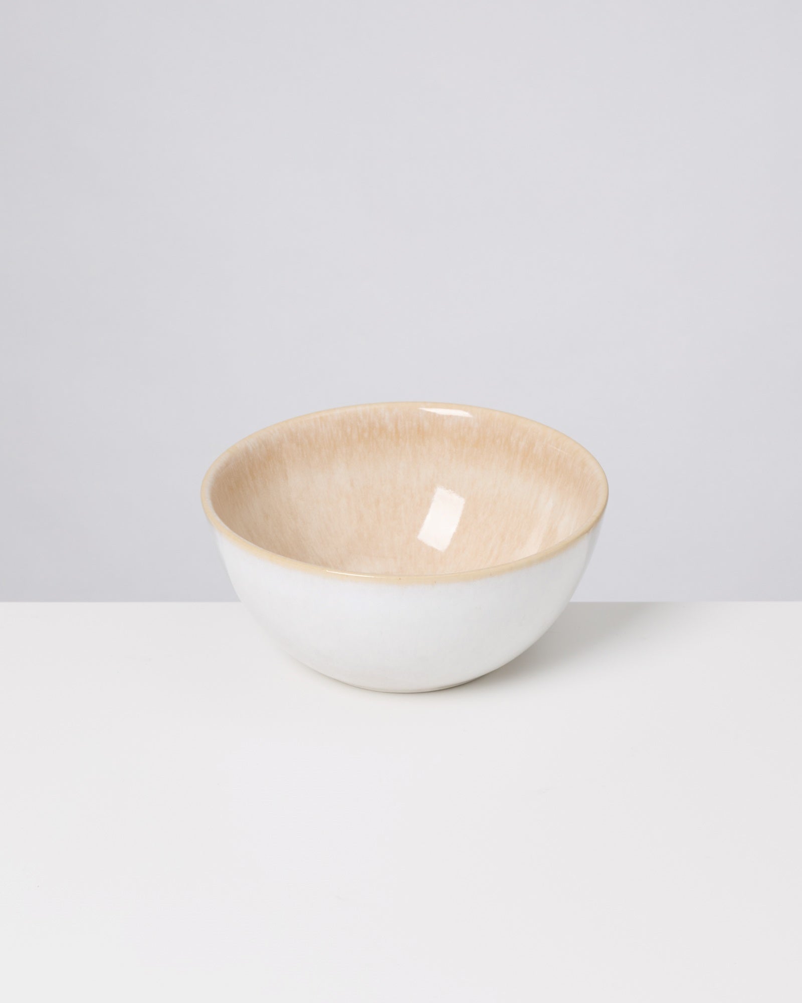 Keramikschale mit beigem Inneren steht auf einem weißen Tisch vor einem grauen Hintergrund.
