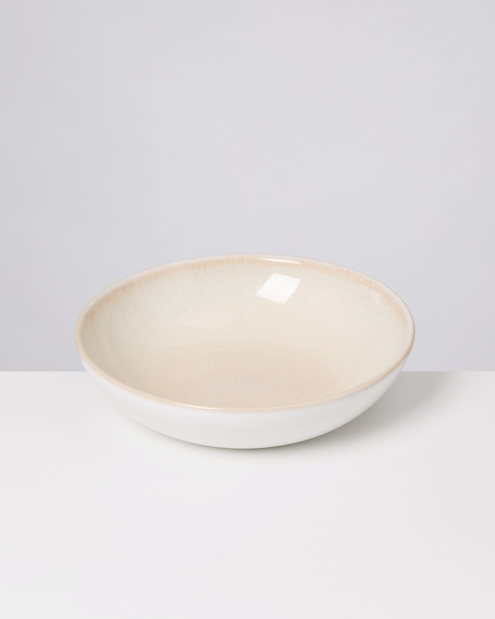 Eine cremefarbene Keramikschale steht auf einem weißen Tisch vor einem hellgrauen Hintergrund.