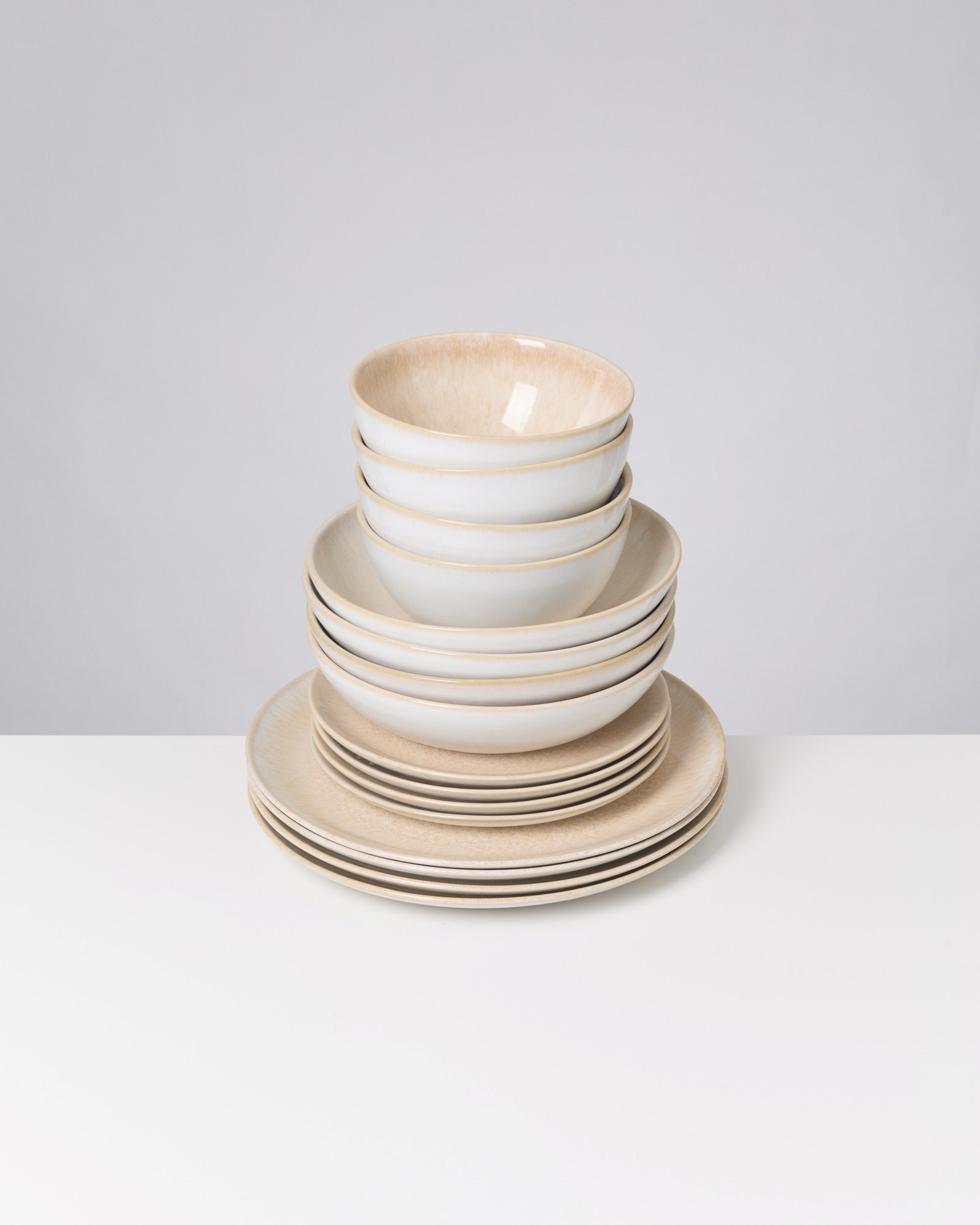 Gestapelte Teller und Schalen in neutralen Tönen auf weißem Hintergrund.