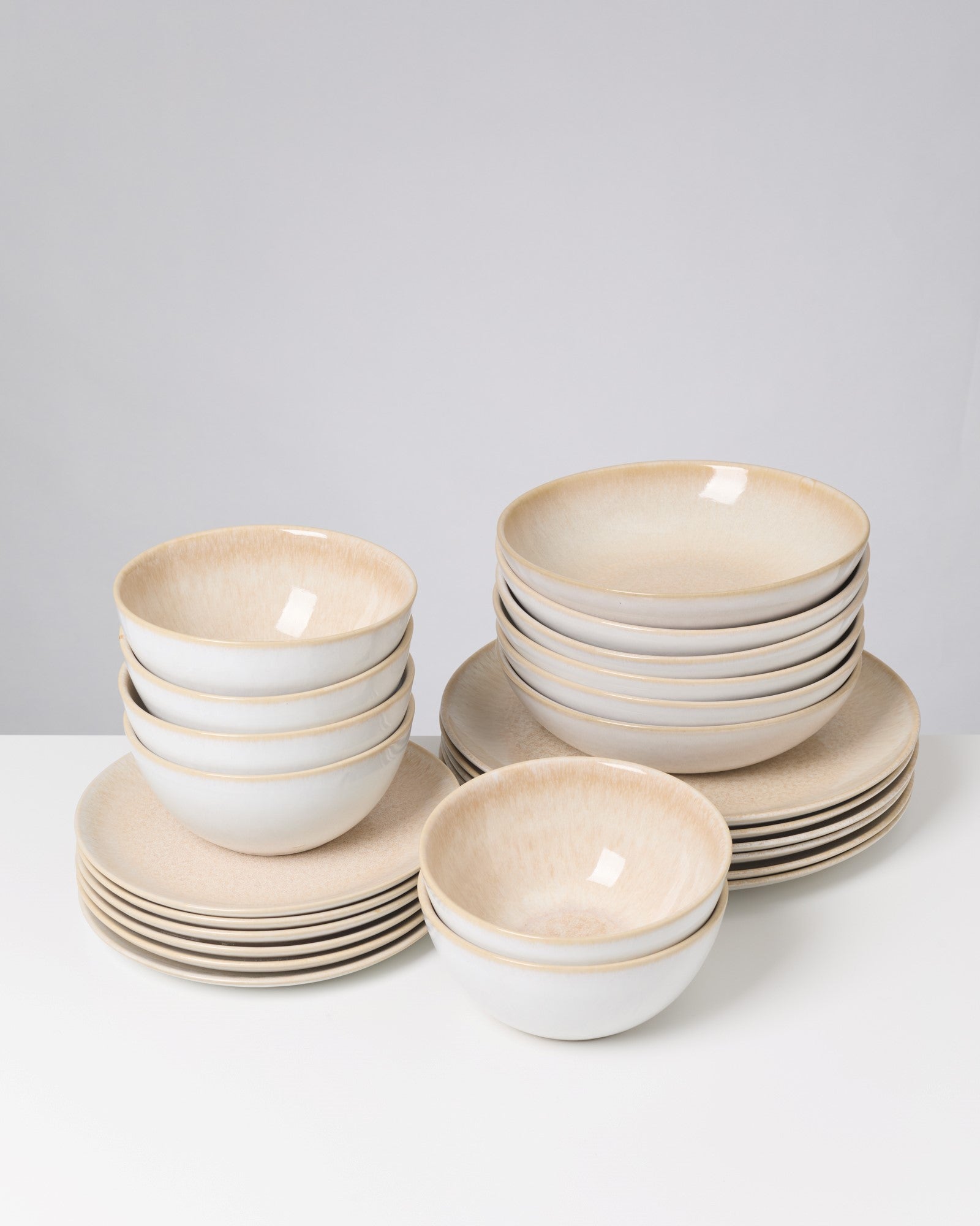 Ein Set aus gestapelten, beigefarbenen Schalen und Tellern steht auf einem weißen Tisch vor grauem Hintergrund.