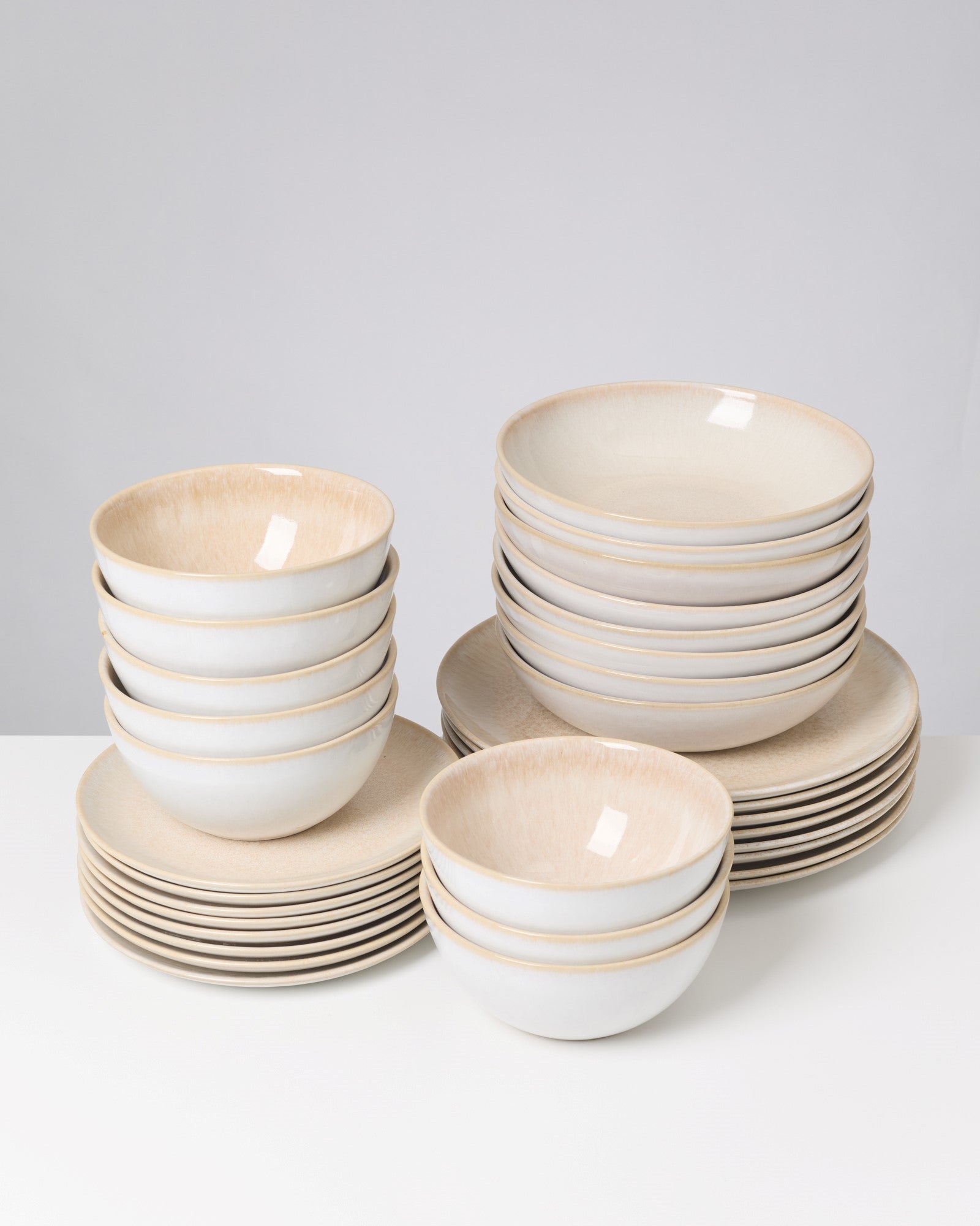 Gestapelte Keramikschalen und -teller in Weiß mit beigem Rand auf einer weißen Oberfläche.