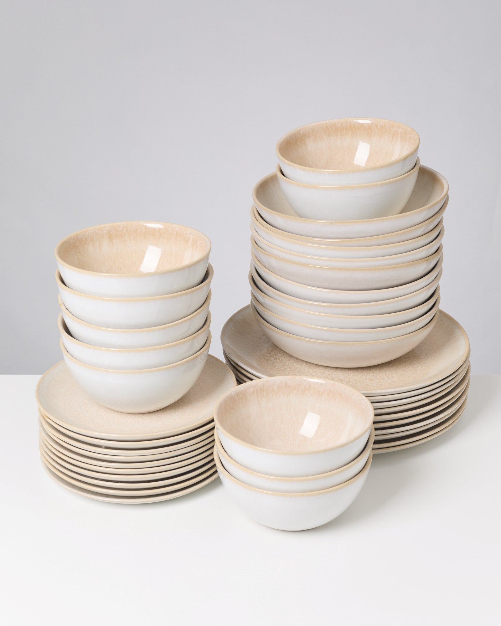 Ein Stapel von weißen Schüsseln und Tellern mit cremefarbenem Rand auf einem weißen Hintergrund.