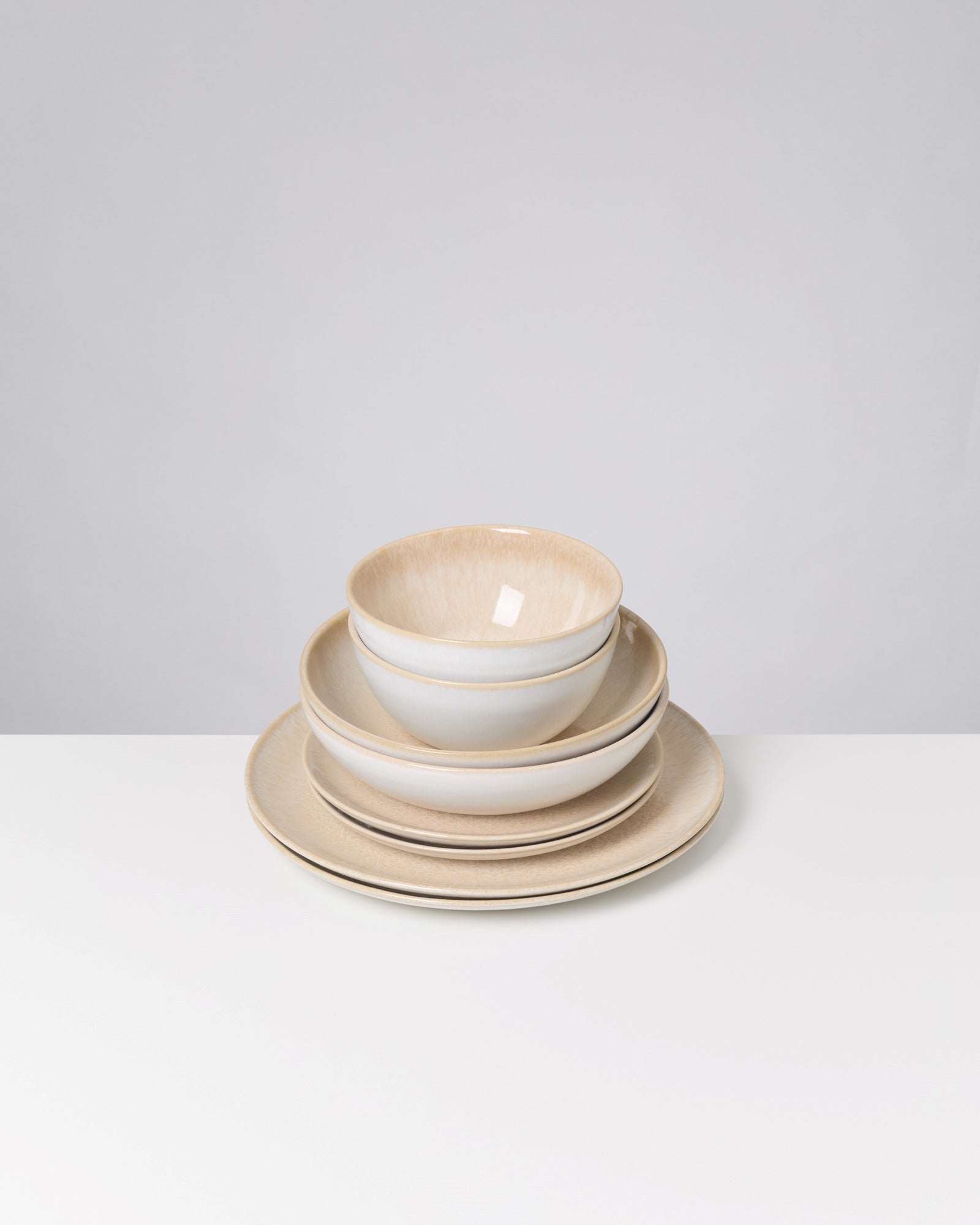 Ein Stapel aus drei Tellern und zwei Schalen in Beige und Weiß auf einem weißen Hintergrund.