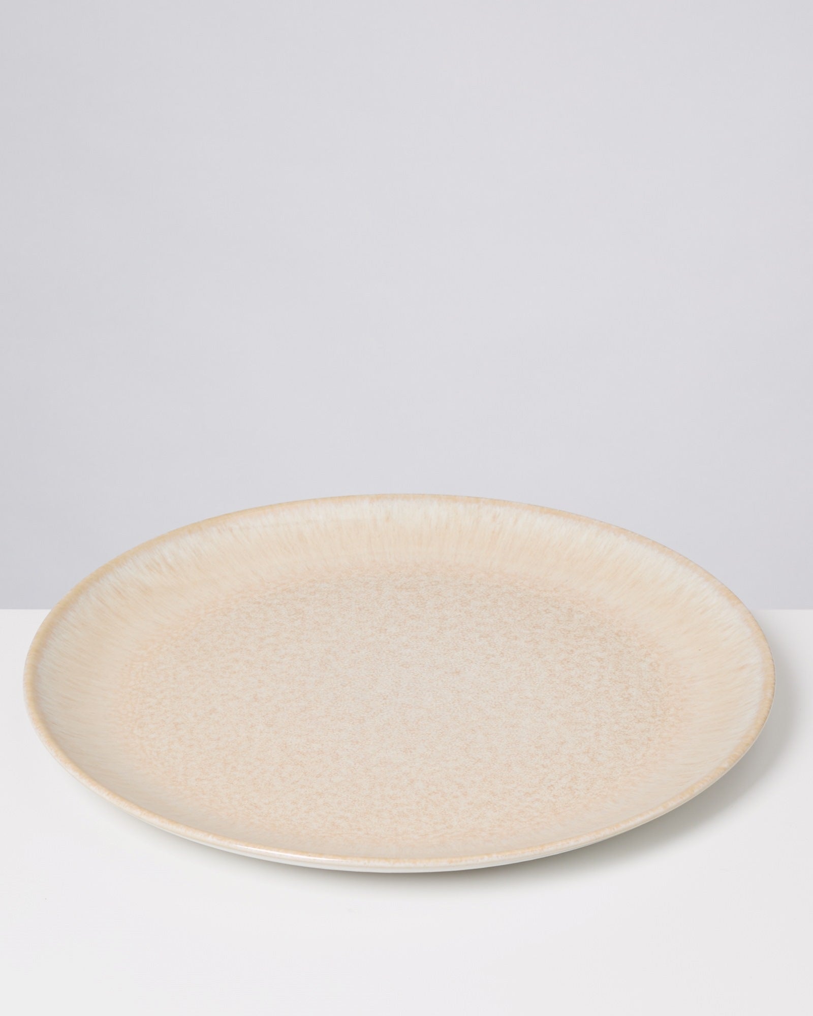 Beiger, runder Keramikteller auf weißer Oberfläche vor grauem Hintergrund.