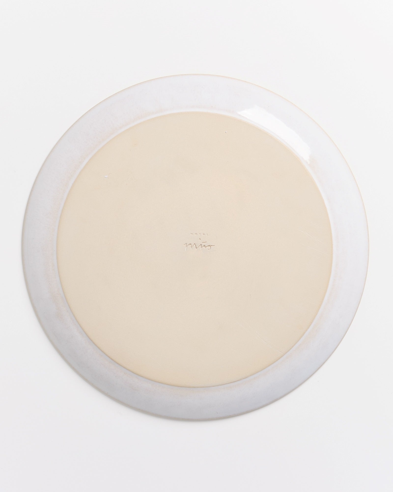 Rückseite eines runden Tellers mit hellem Rand und einer mittig handschriftlichen Markierung auf beigem Untergrund.