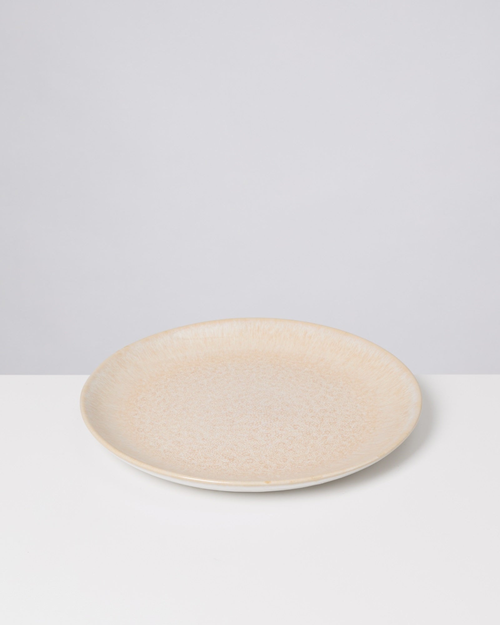 Beiger, runder Teller mit heller Textur auf weißem Hintergrund.