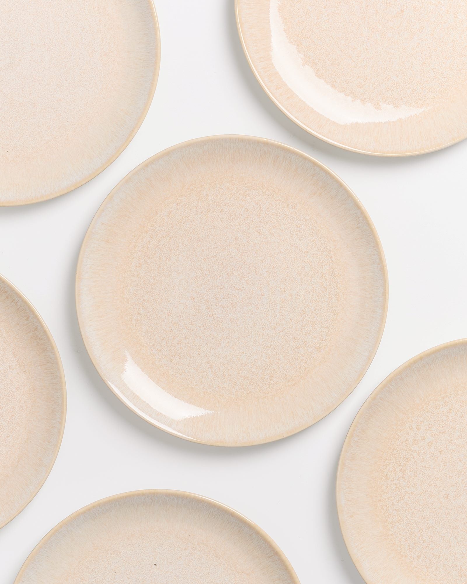 Mehrere beige Keramikteller auf weißem Hintergrund angeordnet.