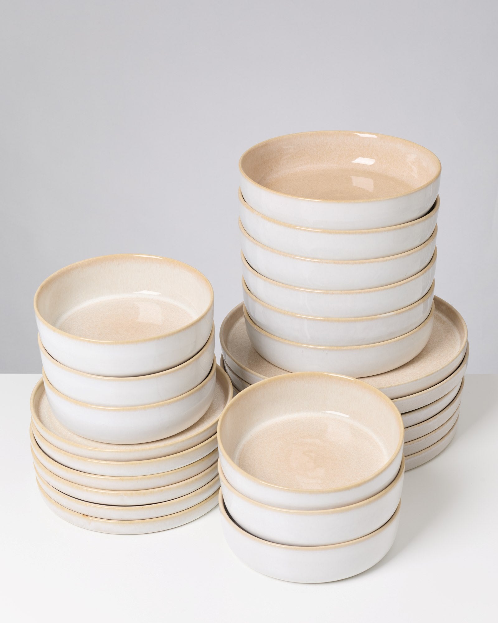 Stapel von weißen Schüsseln mit beigem Rand auf einem weißen Tisch vor grauem Hintergrund.