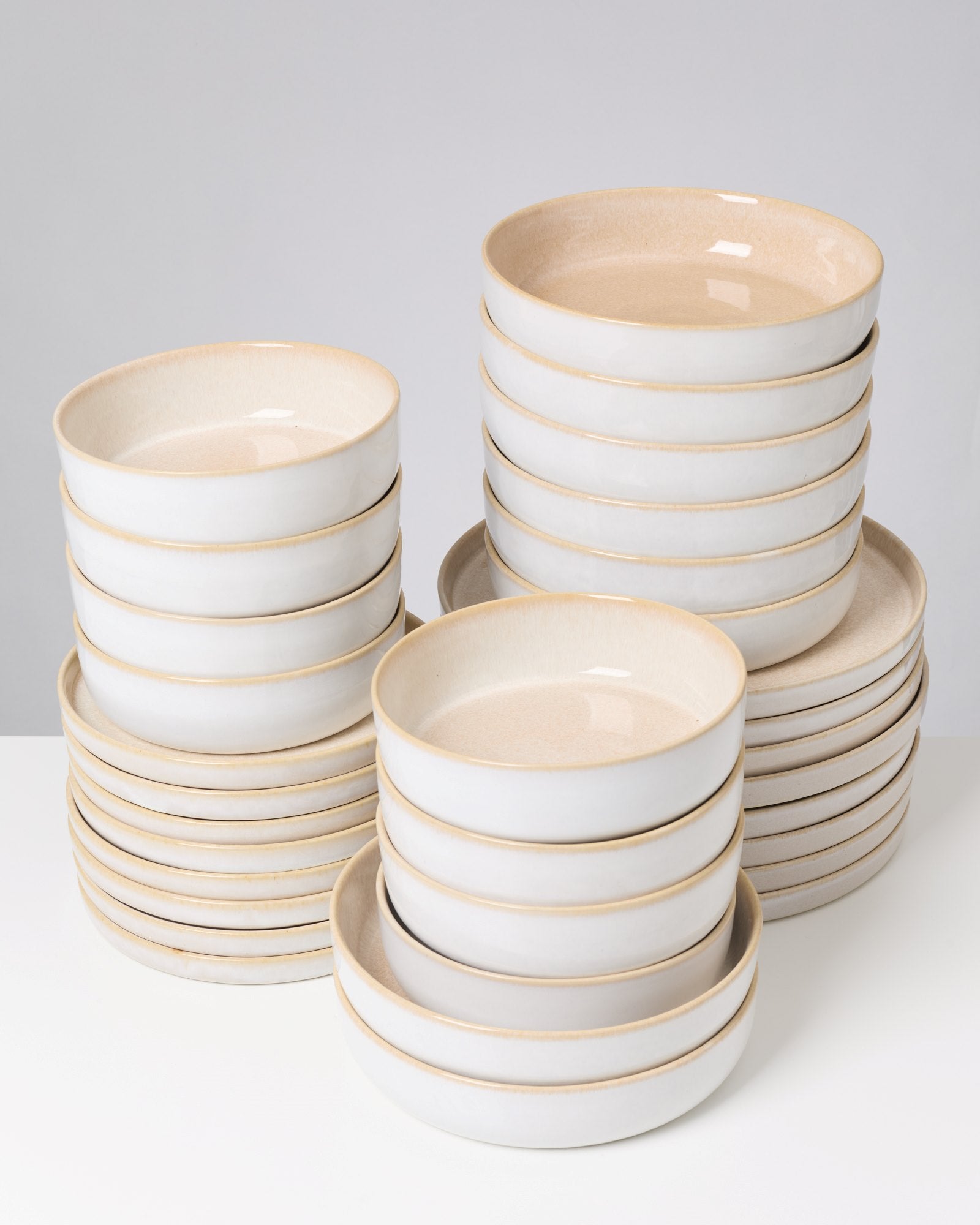 Gestapelte weiße Keramikteller mit einem beigen Rand auf einem weißen Hintergrund.