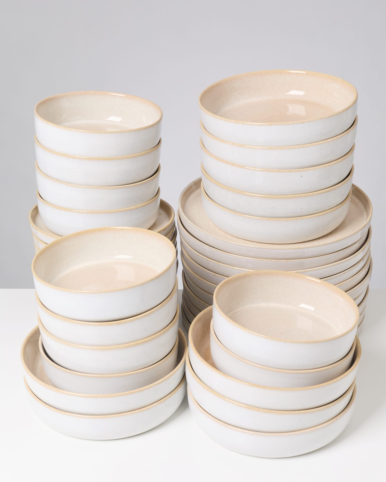 Gestapelte weiße Keramikschüsseln mit beigem Rand auf einem weißen Hintergrund.