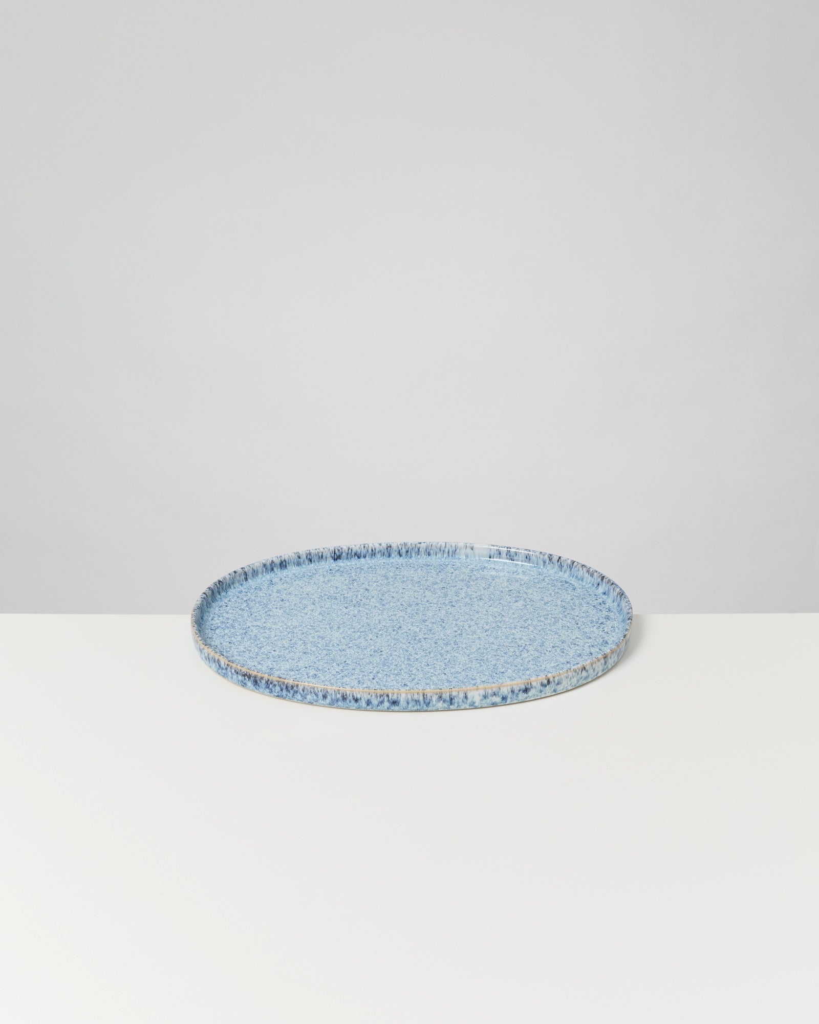 Runder blauer Keramikteller mit gesprenkeltem Muster auf weißem Untergrund.