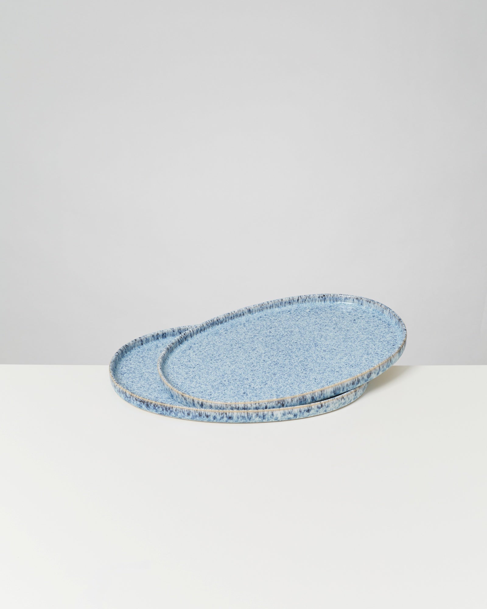 Zwei blaue, ovale Platten mit gesprenkeltem Muster auf einer weißen Oberfläche vor neutralem Hintergrund.