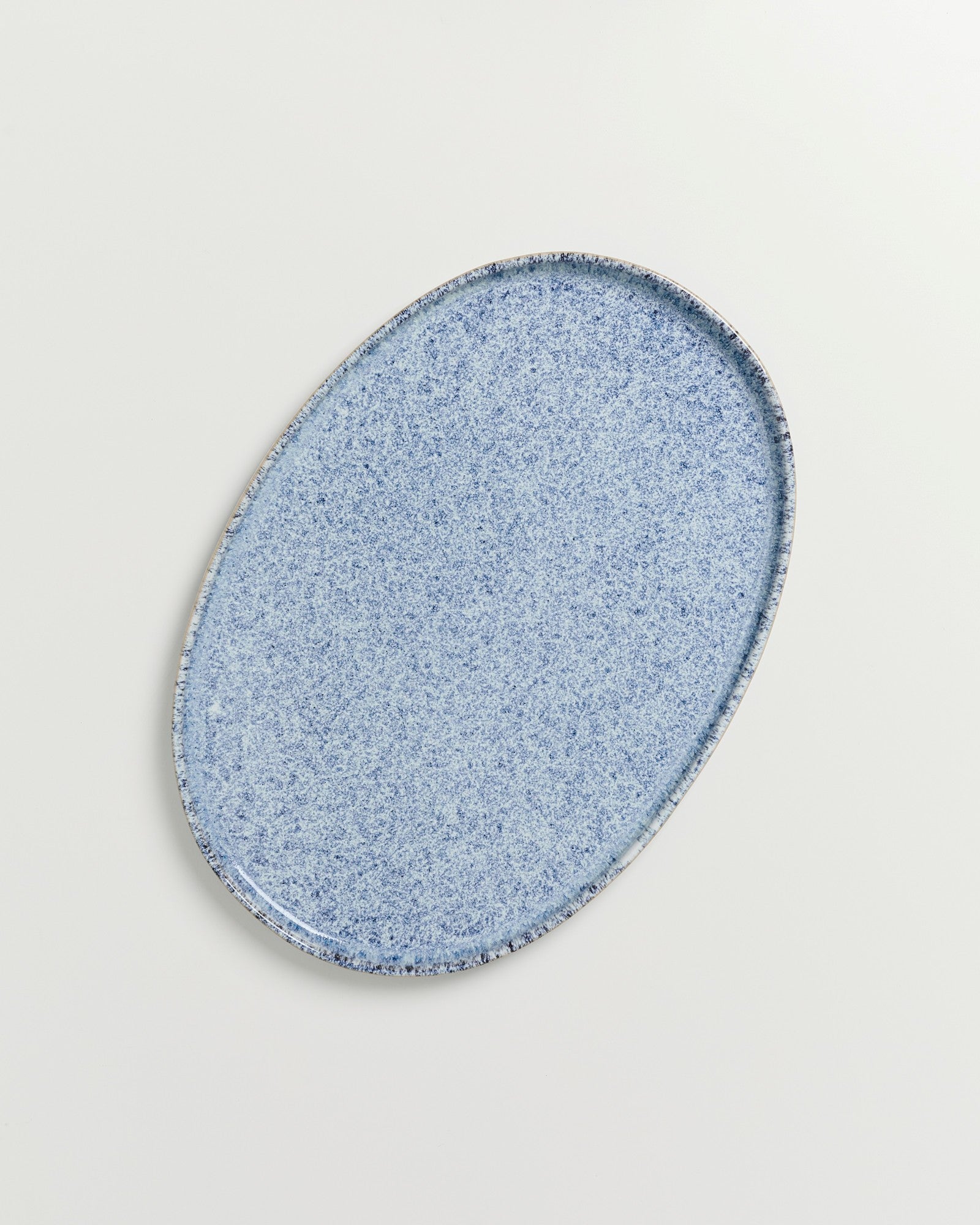 Ovale hellblaue Keramikplatte mit gesprenkelter Oberfläche auf hellem Hintergrund.