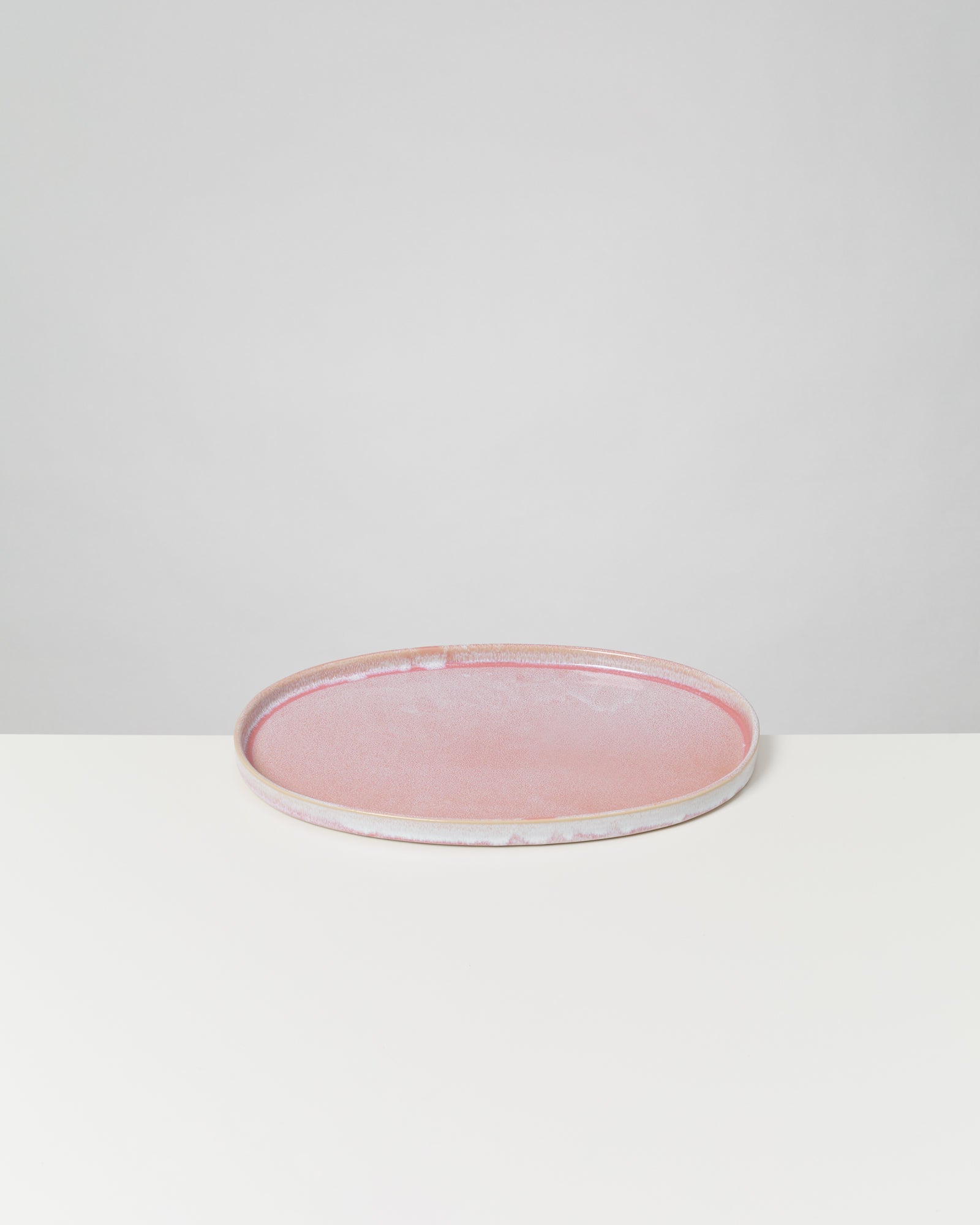 Rosa Keramikteller auf weißem Tisch vor einem grauen Hintergrund.