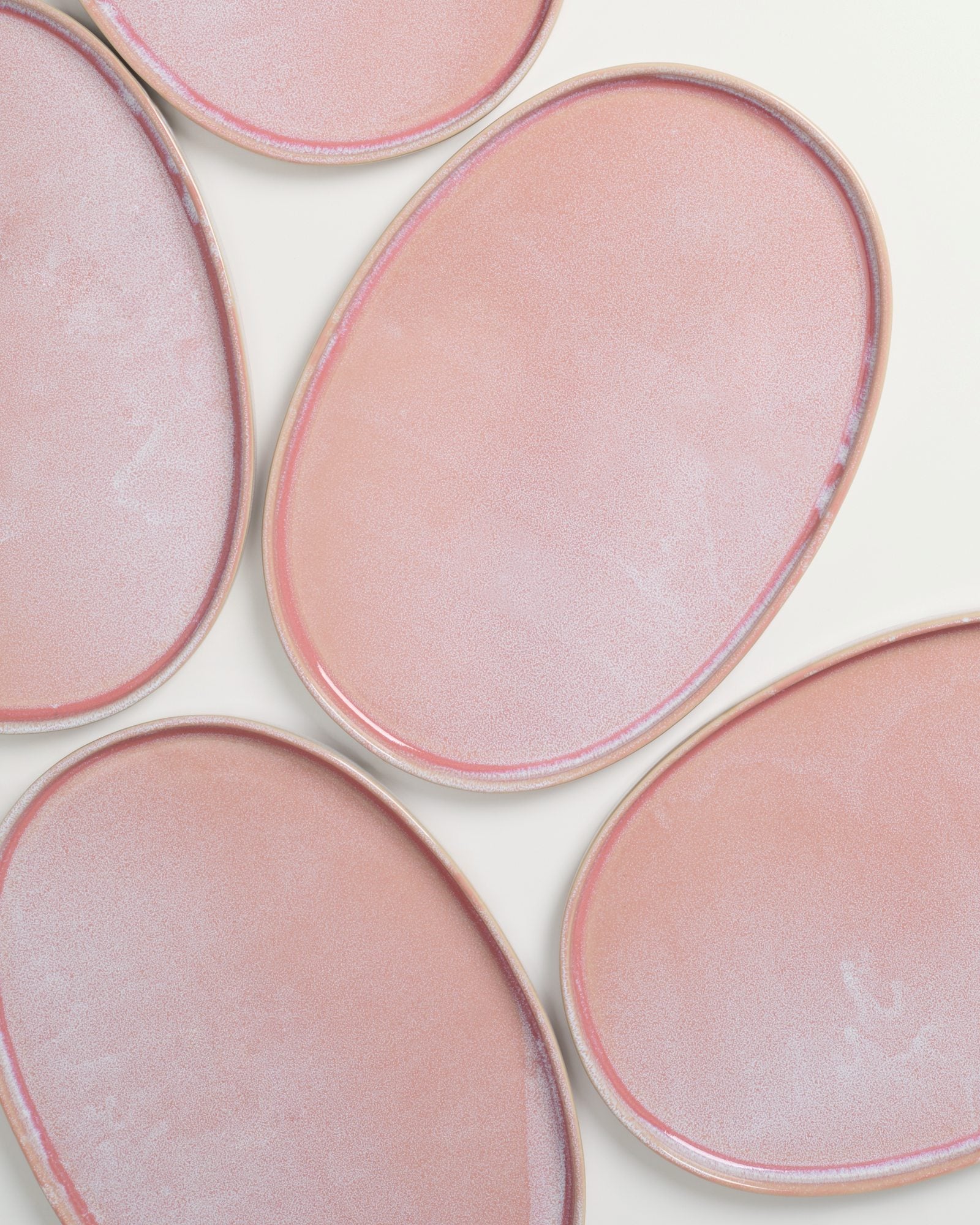 Sechs ovale, rosa Keramikteller mit glattem, glänzendem Finish auf weißem Hintergrund.