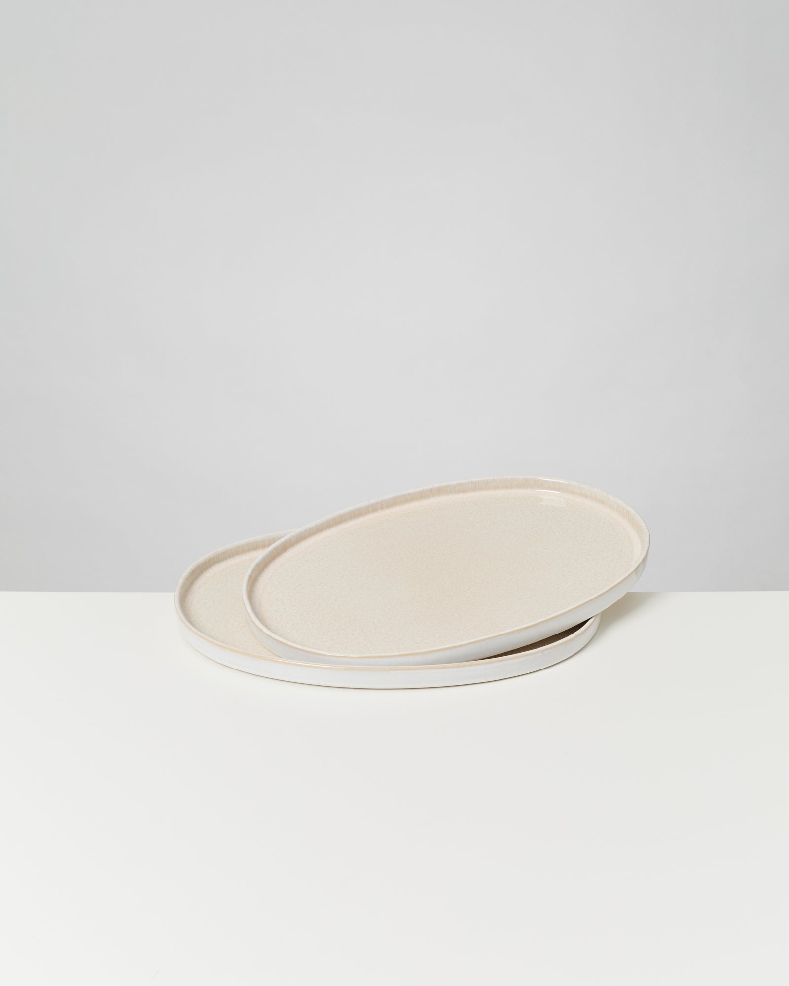 Zwei übereinanderliegende ovale Teller auf einer weißen Oberfläche.