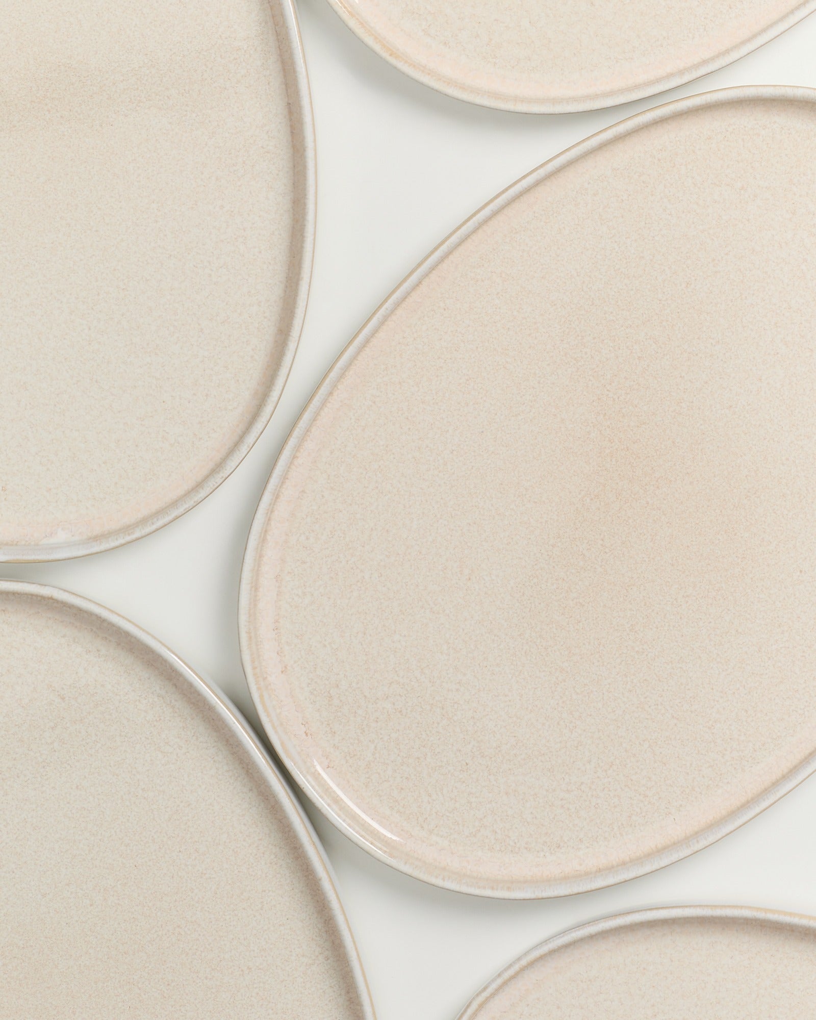 Mehrere flache, ovale, beige Keramikteller liegen auf einer weißen Oberfläche.