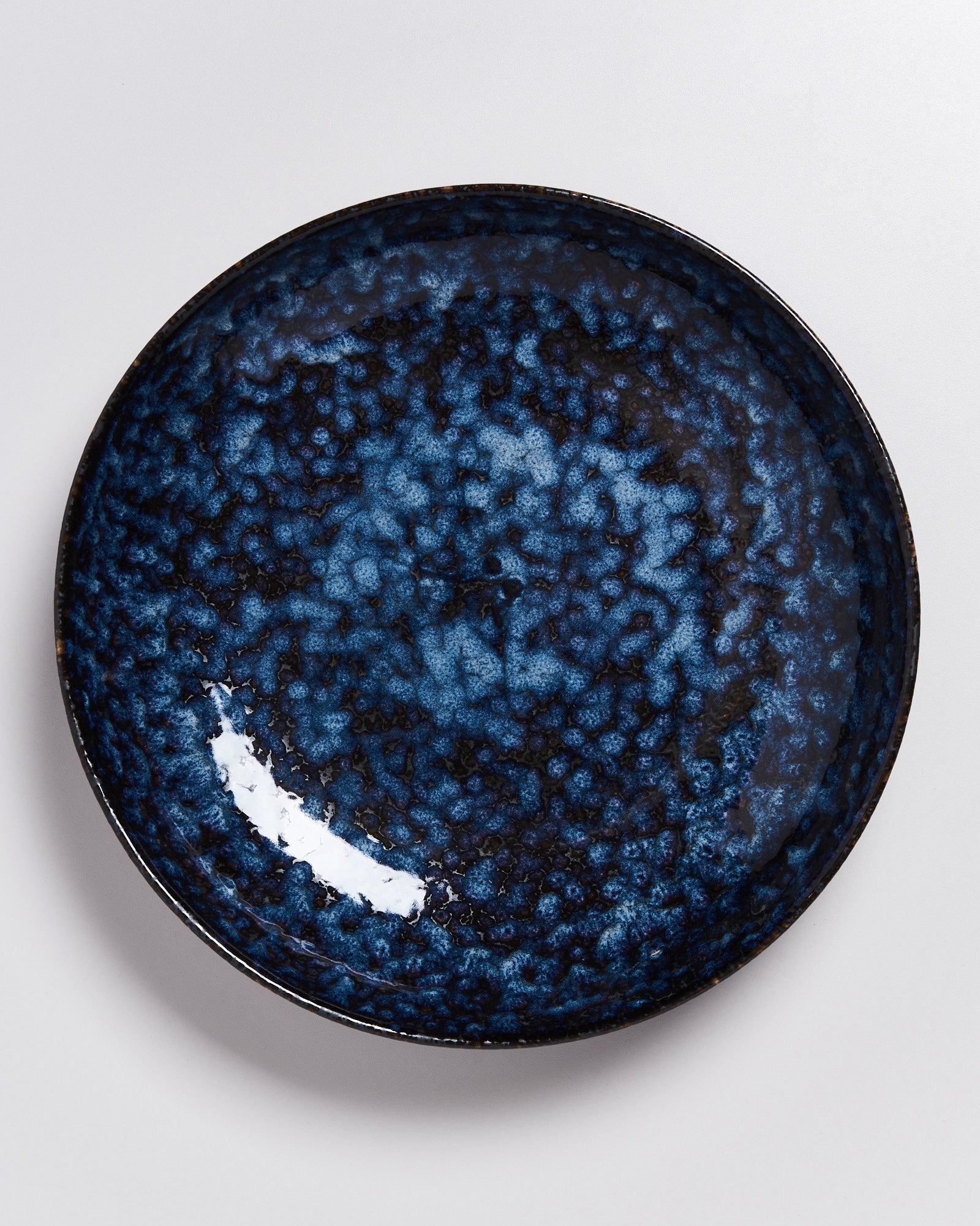 Blauer Keramikteller mit einem unregelmäßigen, marmorierten Muster auf einem weißen Hintergrund.
