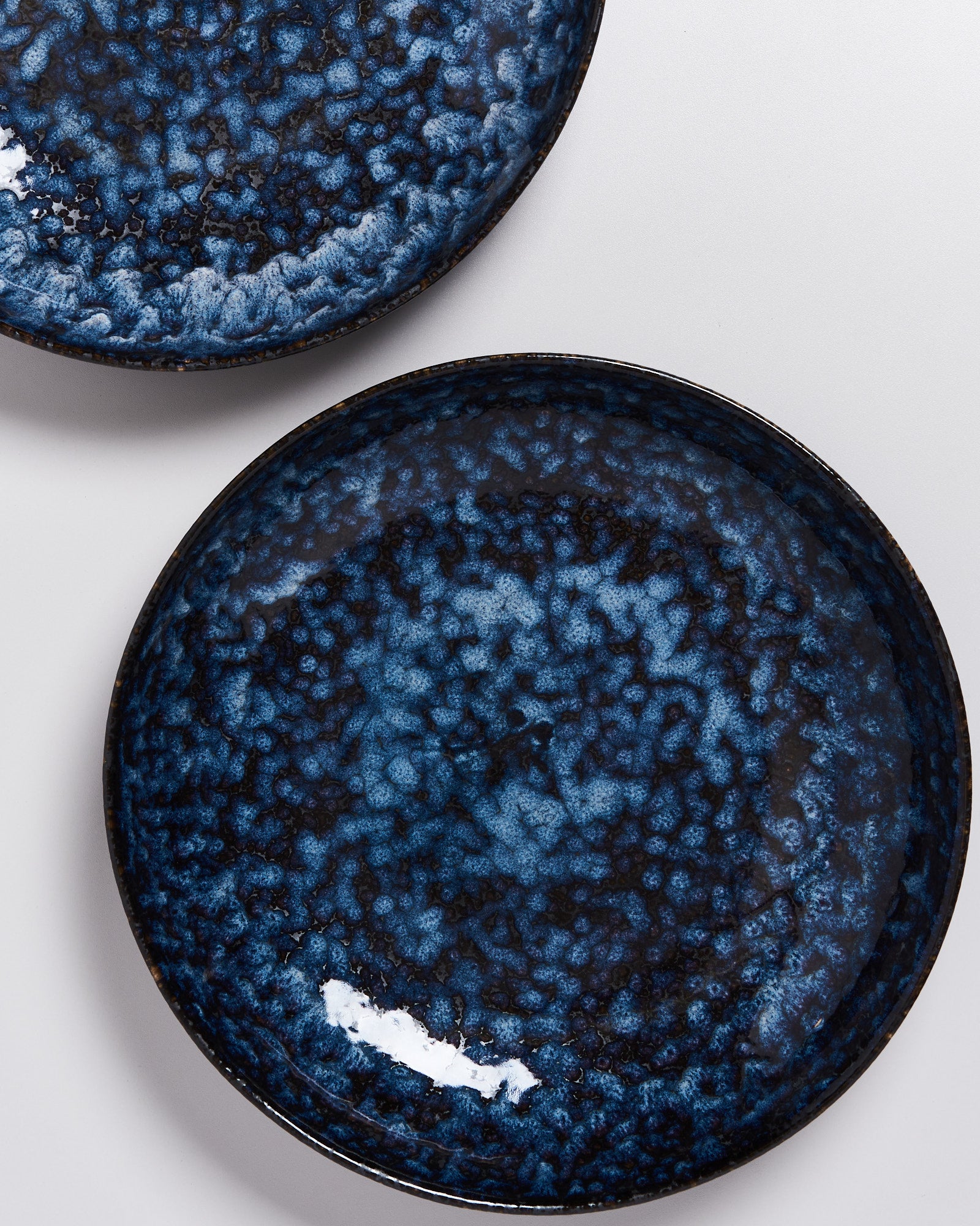 Zwei runde, blaue Keramikteller mit marmoriertem Muster auf einer weißen Oberfläche.