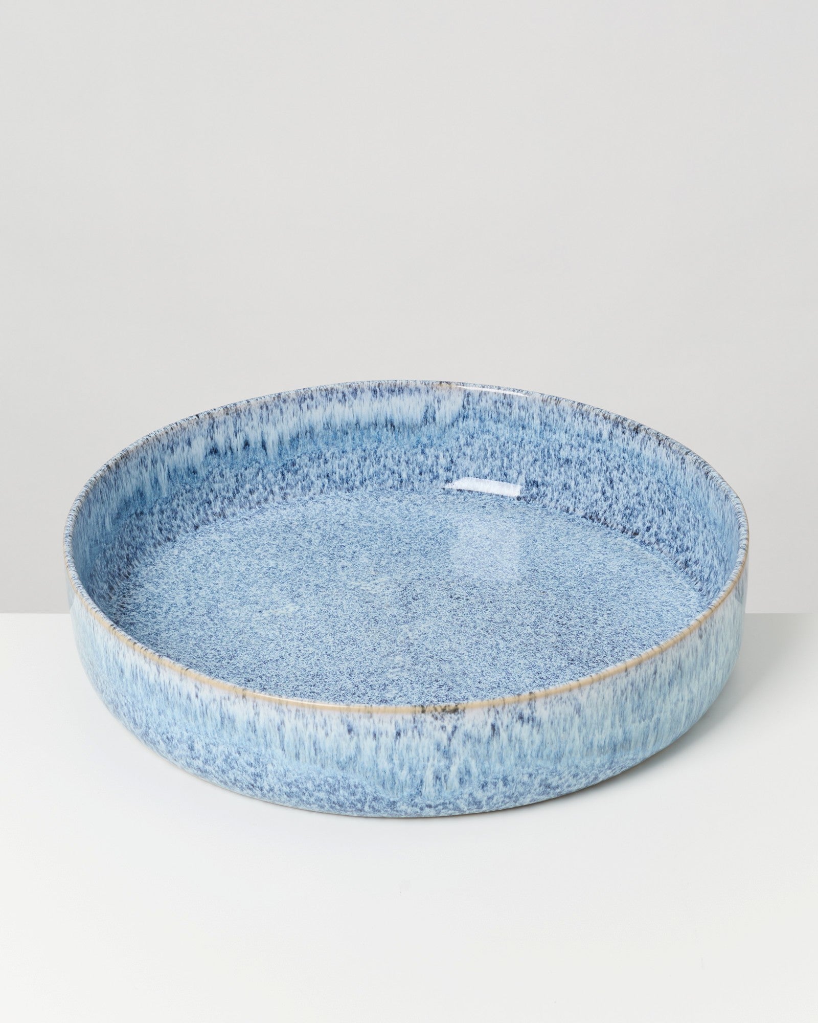 Große, flache, runde Schale aus hellblauem Keramik mit gesprenkeltem Muster auf einem weißen Hintergrund.