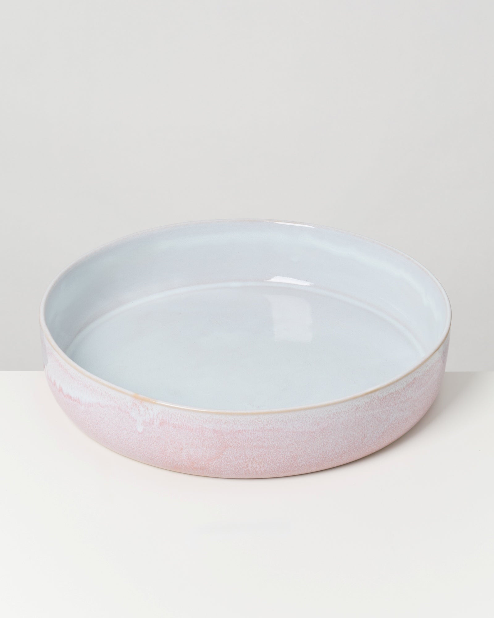 Runde, flache Keramikschale in Pastellfarben auf einem weißen Untergrund.