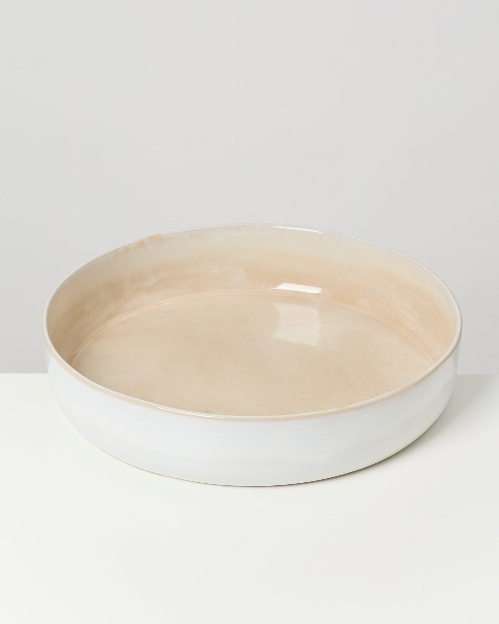 Beiger, flacher Keramikteller mit glänzender Oberfläche steht auf einem weißen Hintergrund.