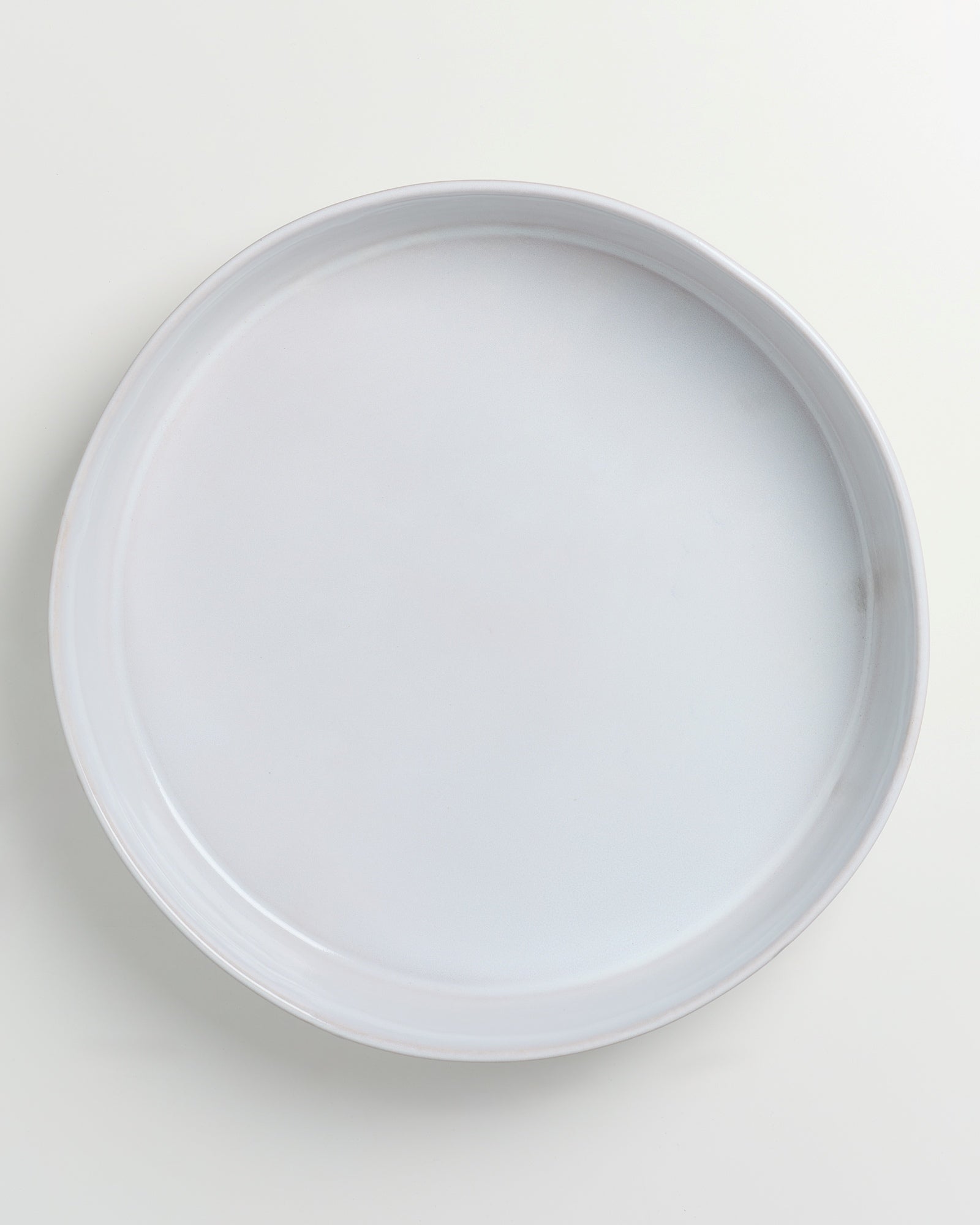 Ein weißer, runder leerer Teller auf einem hellen Hintergrund.