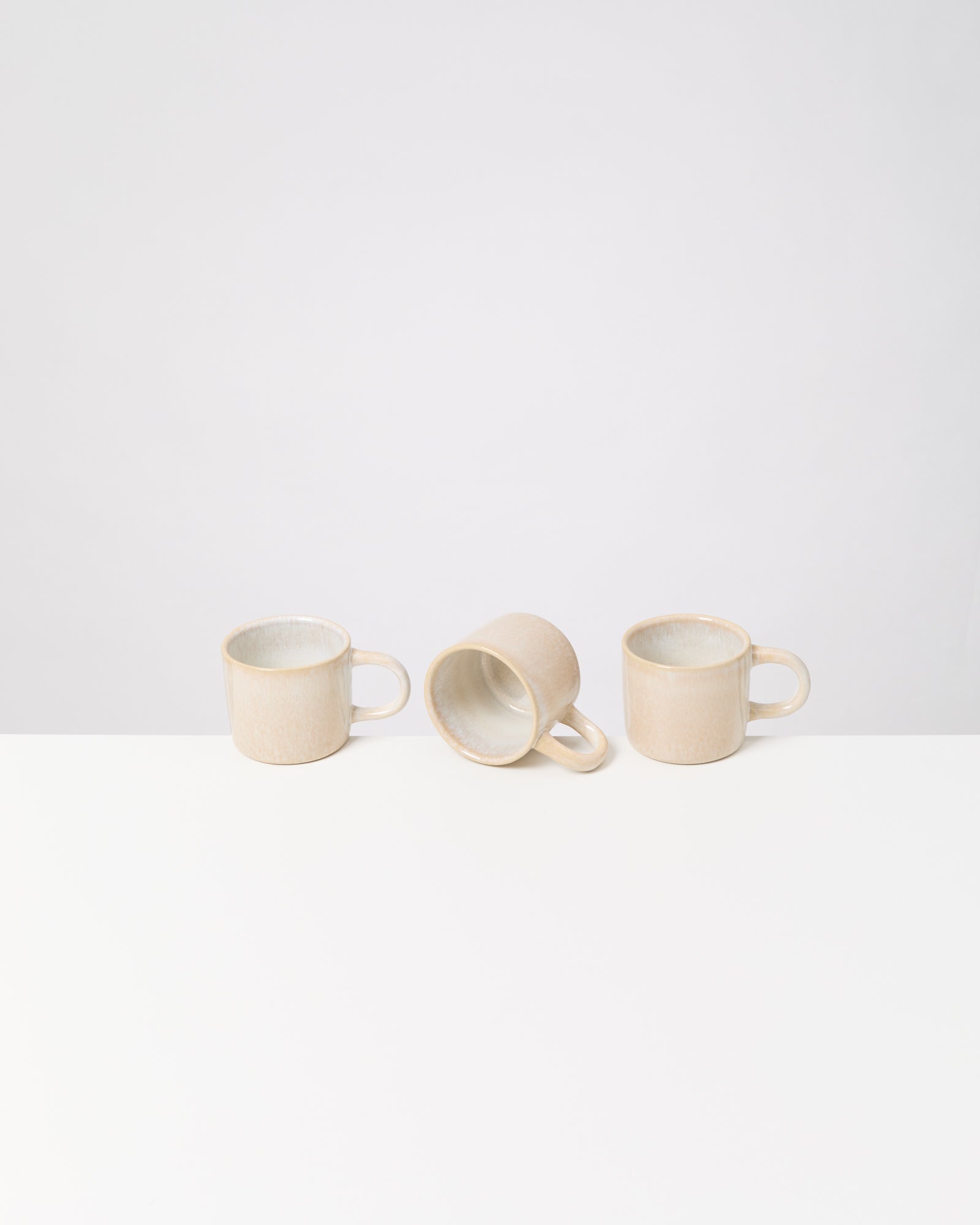 Drei beige Tassen auf einem weißen Tisch, eine liegt auf der Seite.