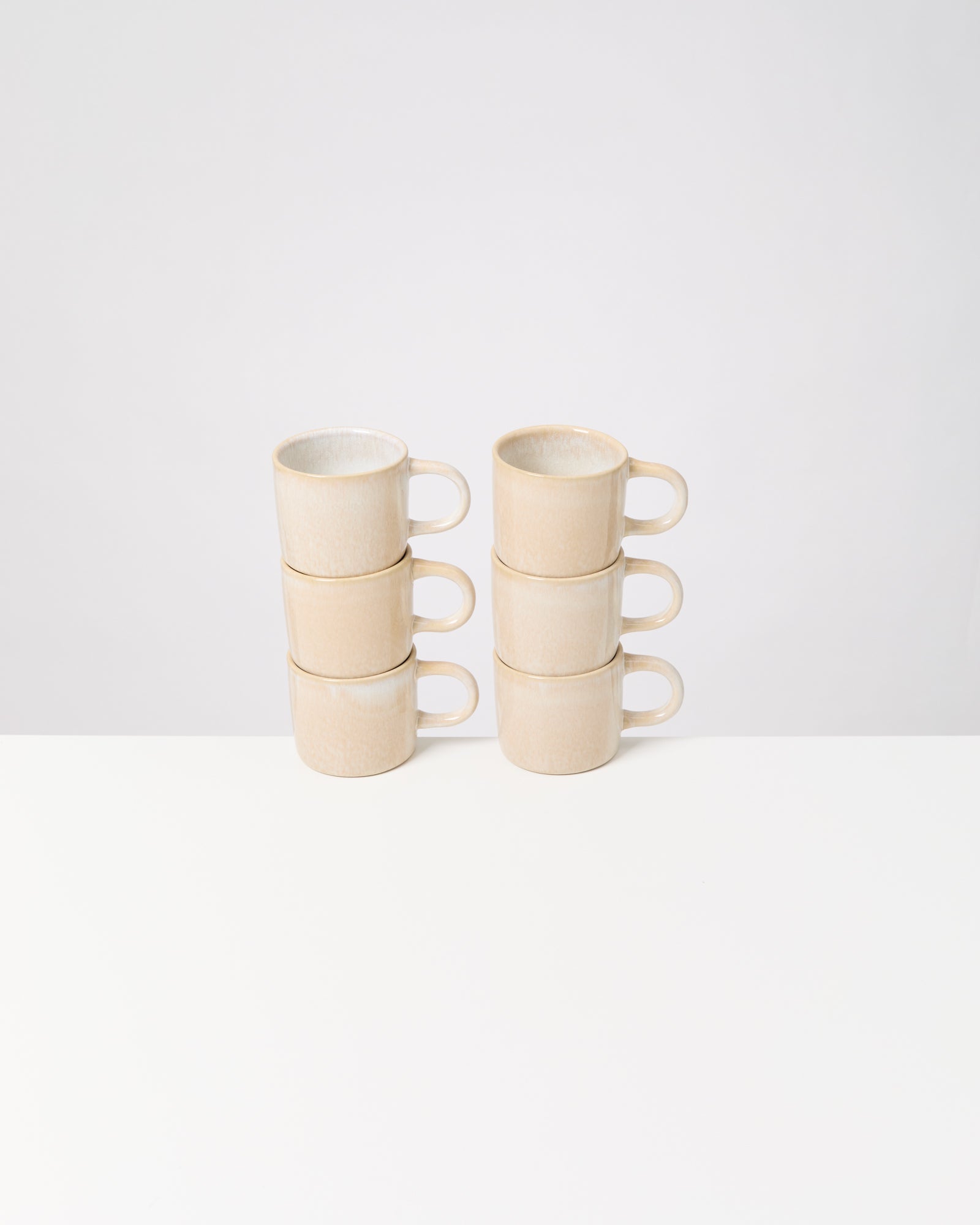 Sechs gestapelte, beige Kaffeetassen auf einem weißen Tisch vor weißem Hintergrund.