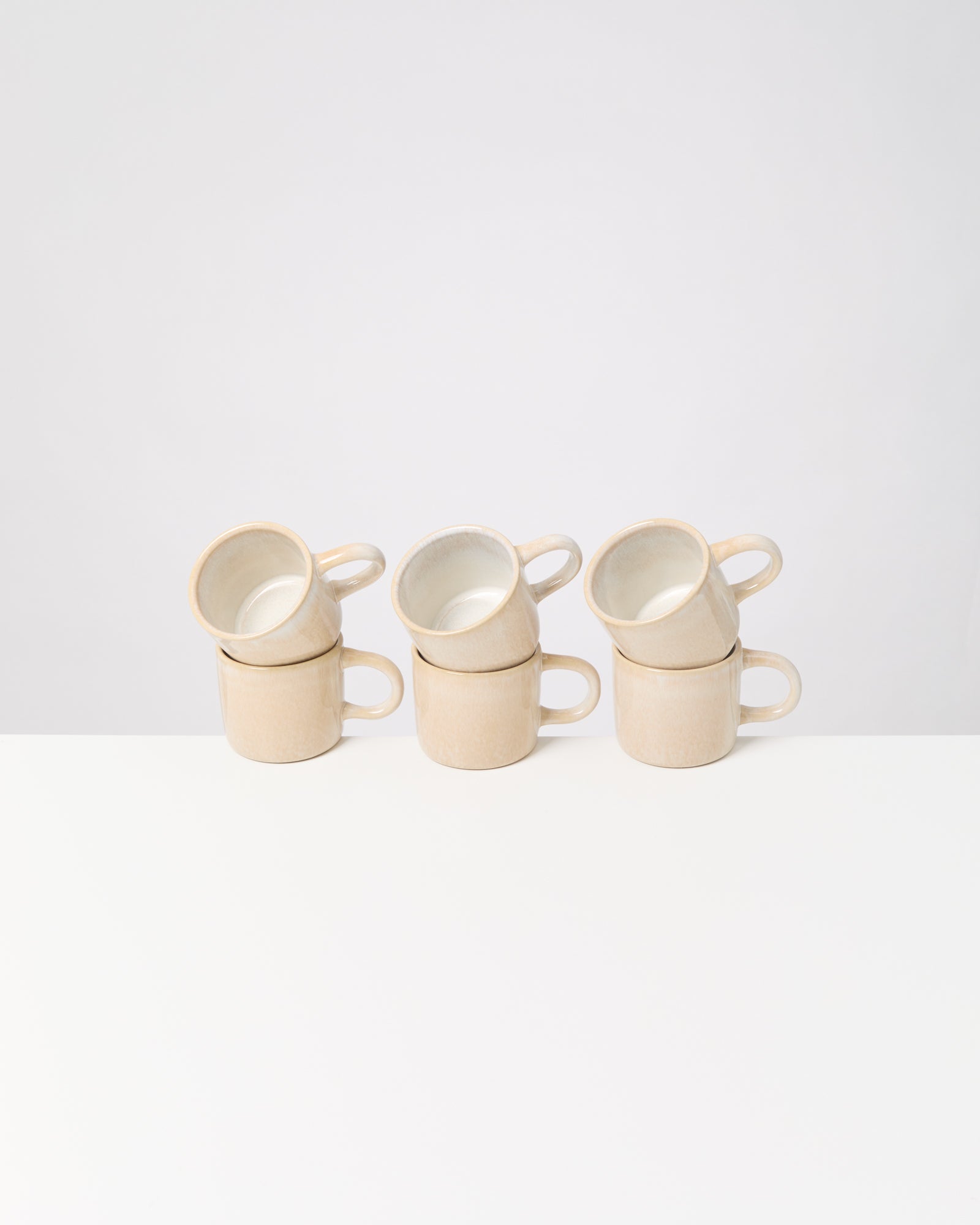 Drei Stapel aus je zwei beigen Tassen stehen auf einem weißen Tisch vor hellem Hintergrund.
