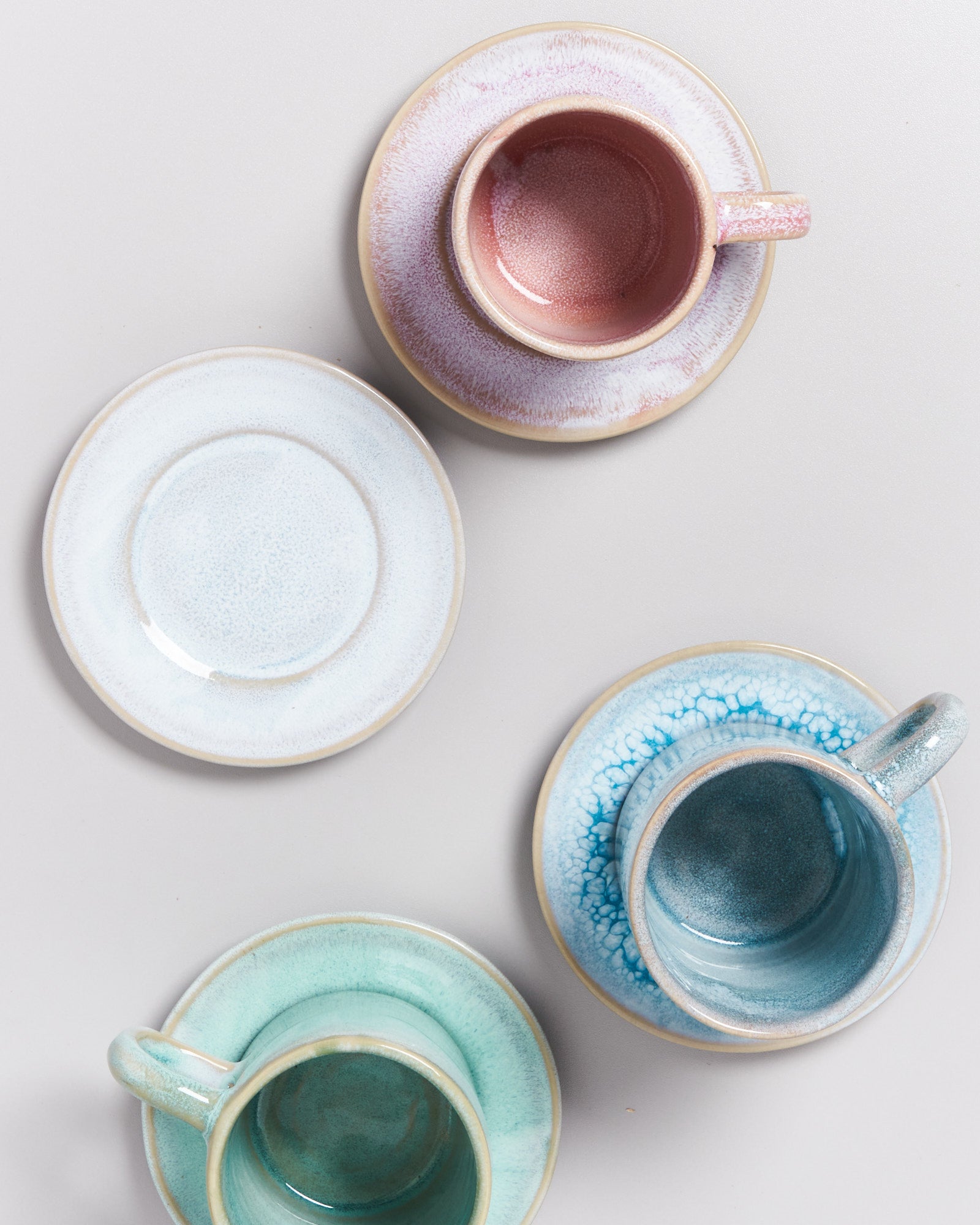 Vier Tassen mit Untertassen in verschiedenen Pastelltönen auf einem hellen Hintergrund.