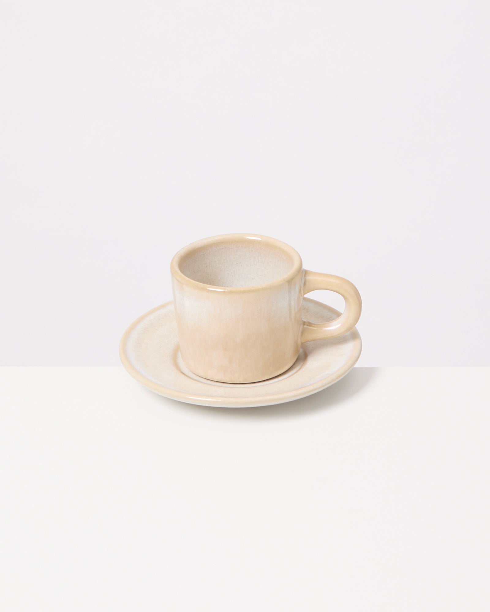 Beige Tasse mit Untertasse auf weißem Hintergrund.