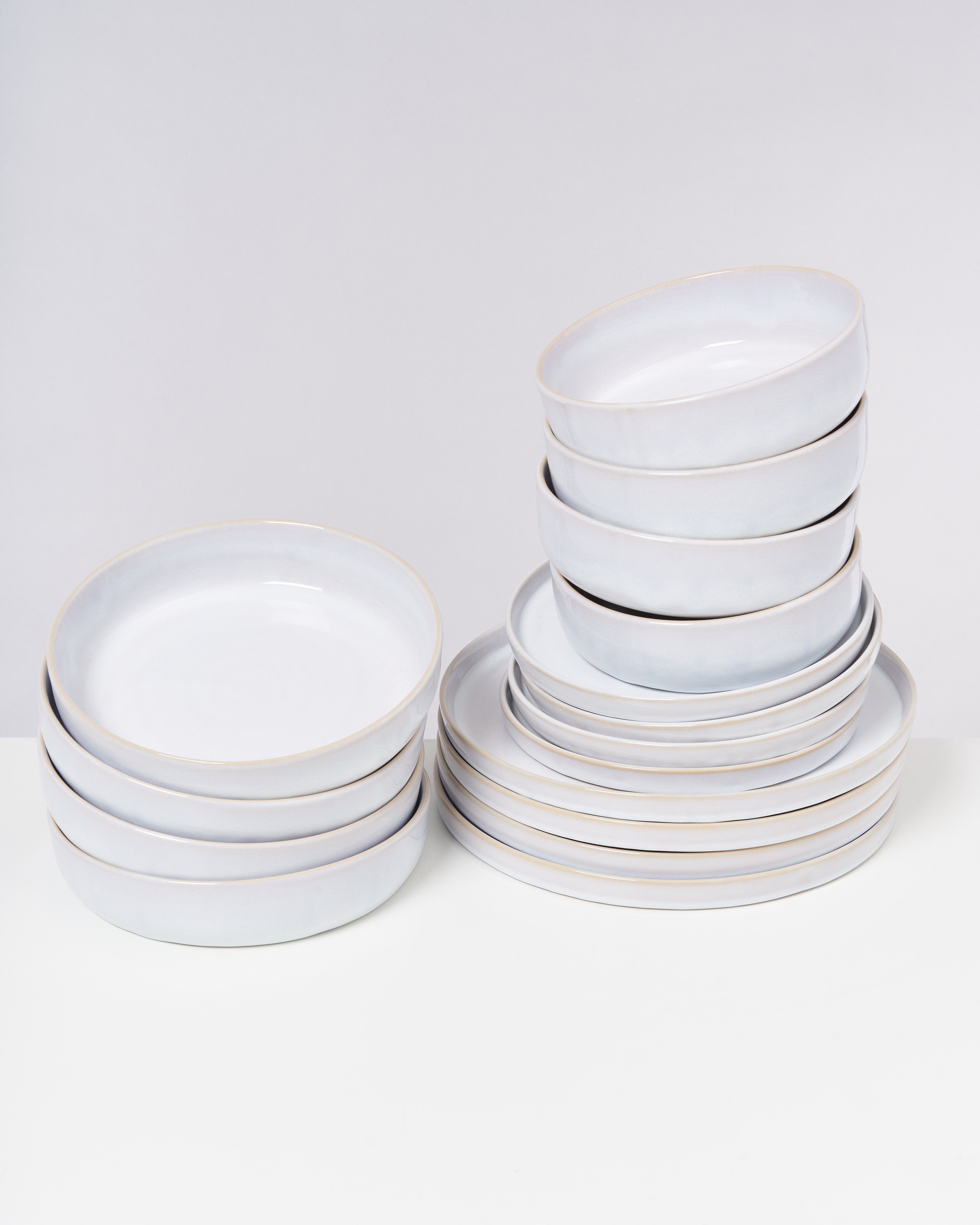 Zwei Stapel mit weißen, runden Keramiktellern vor einem grauen Hintergrund.