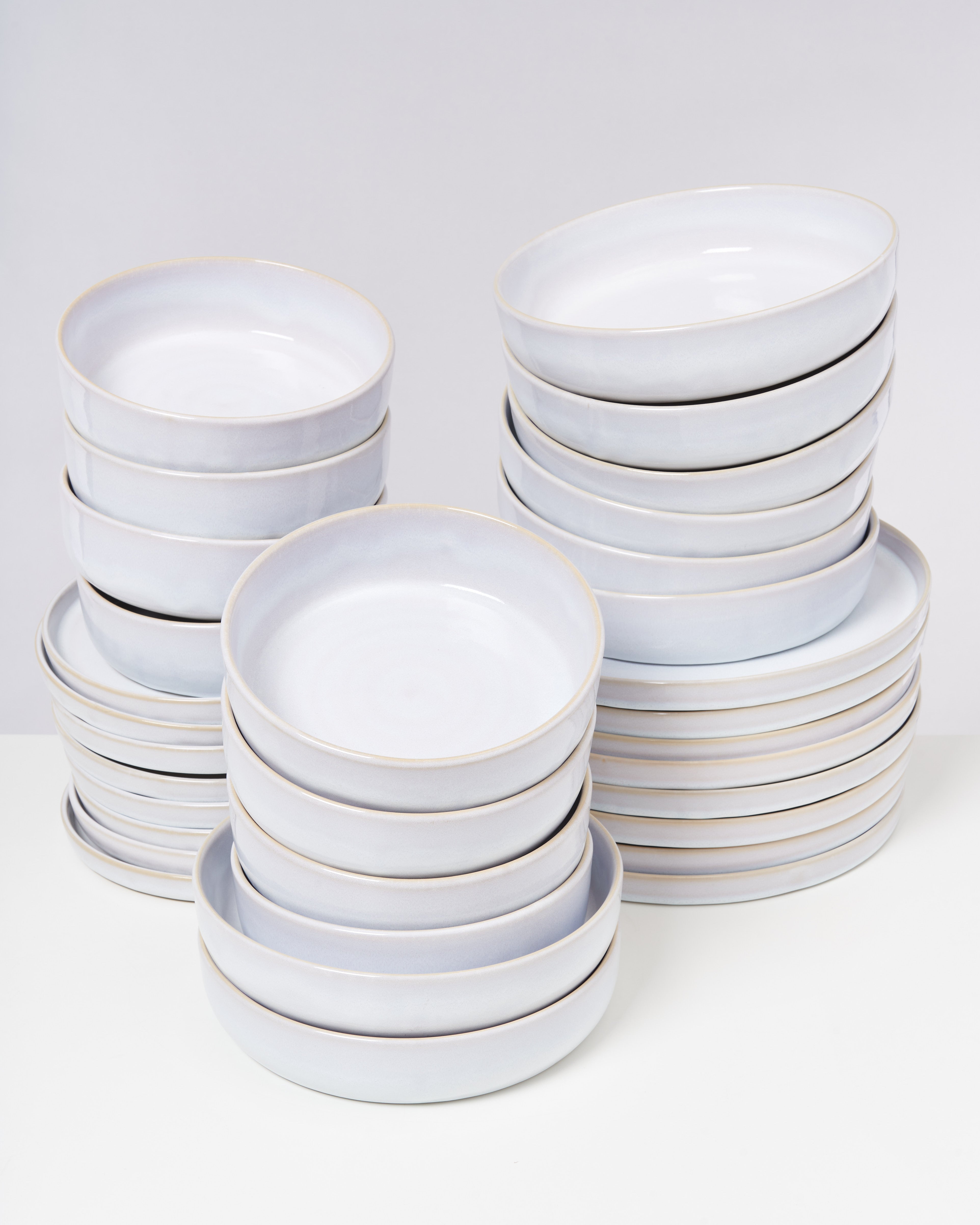 Stapel von weißen, flachen und tiefen Tellern auf einem weißen Hintergrund.