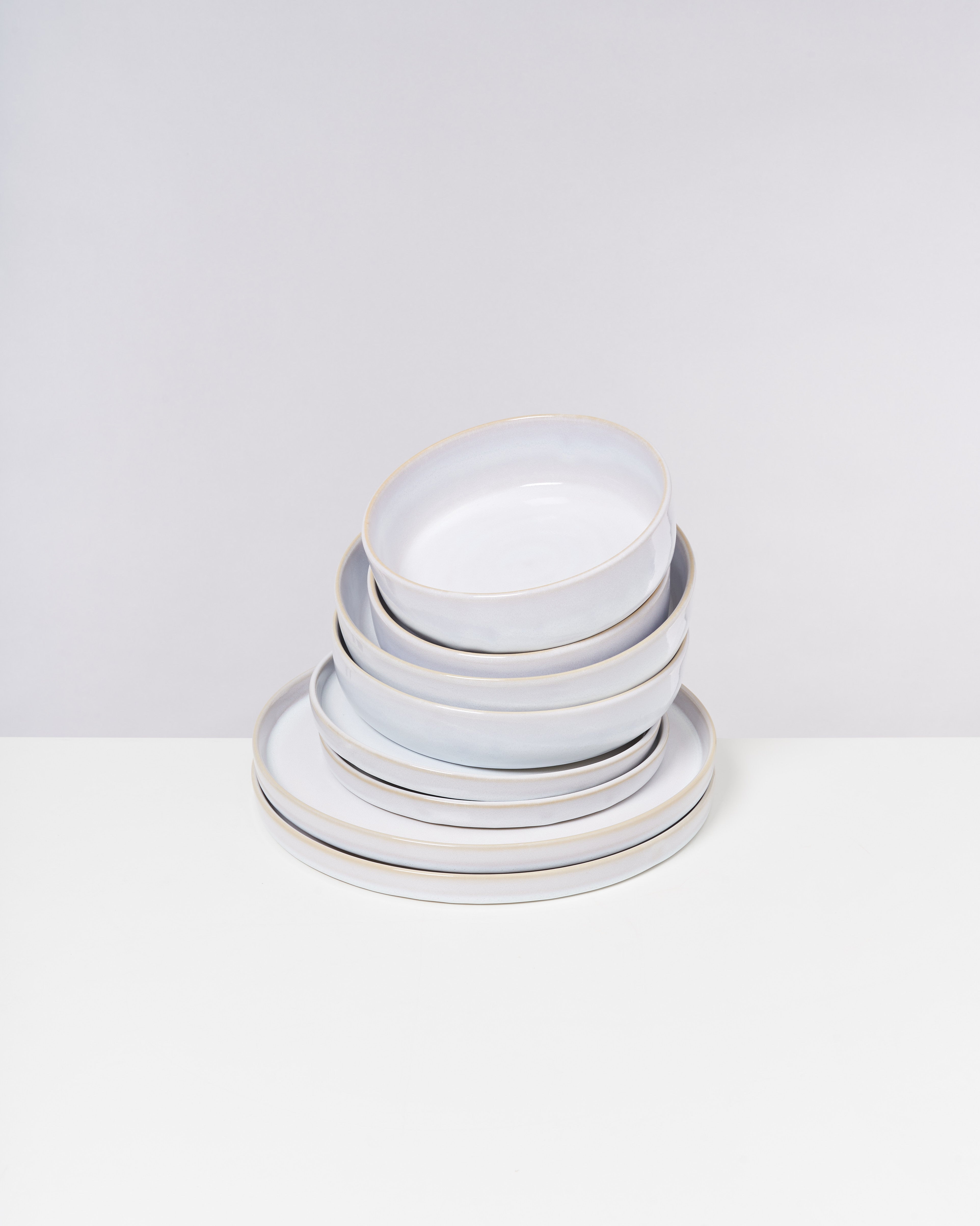 Ein Stapel weißer Teller mit leicht bläulichem Schimmer auf einem weißen Hintergrund.